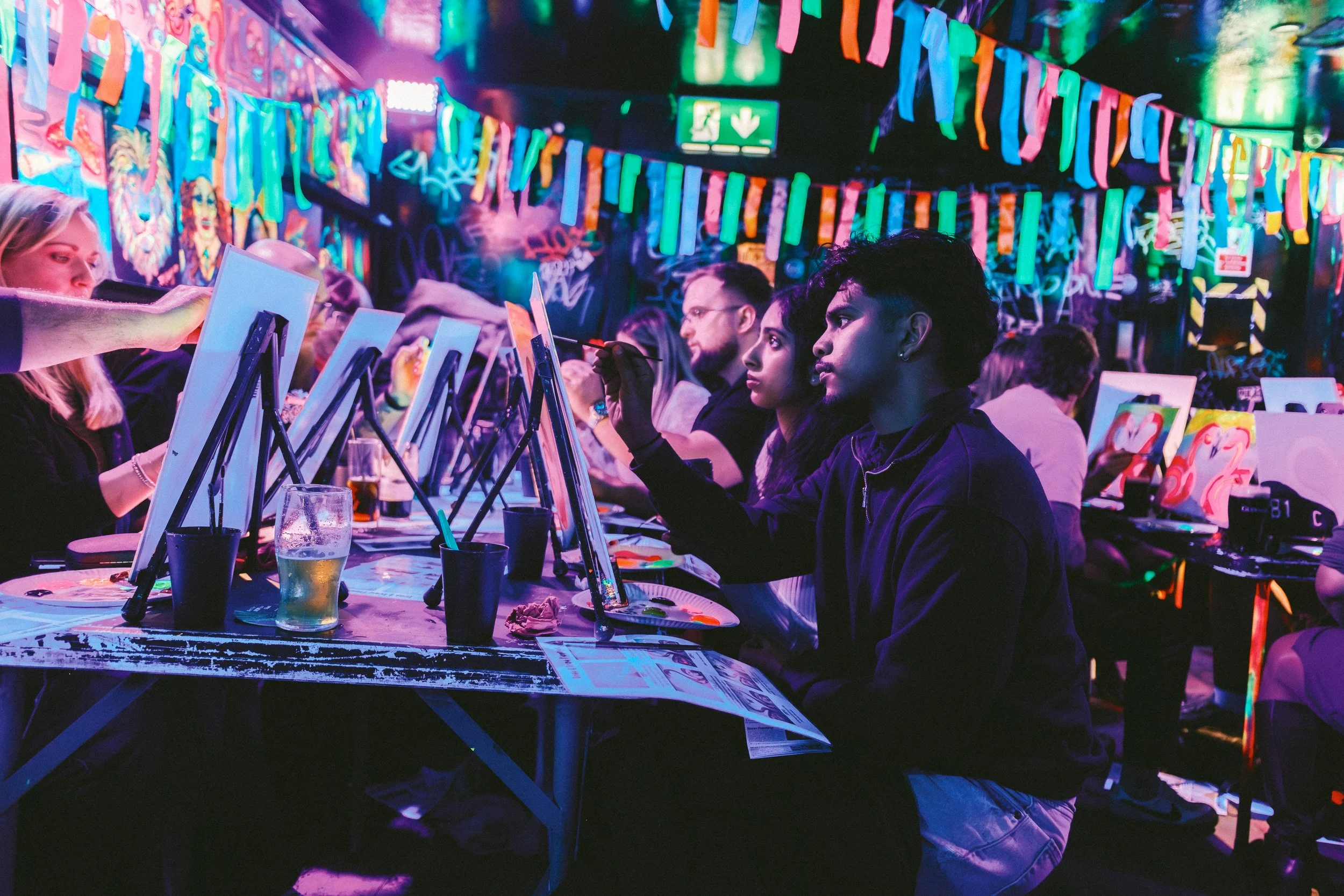 Laughing people with neon paint in their faces, painting a canvas.