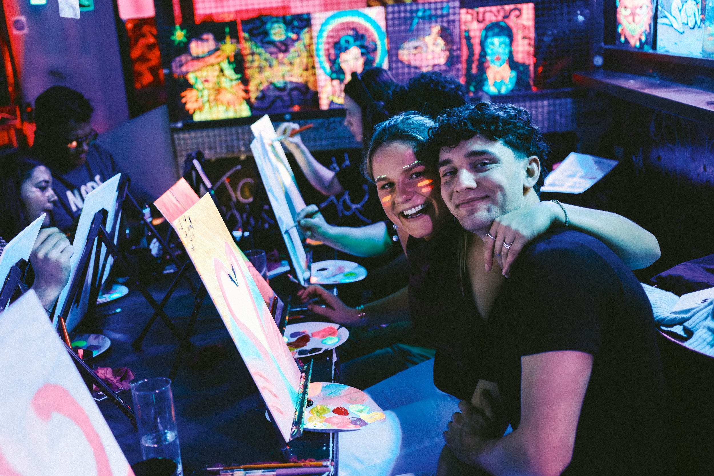 Many easels with canvas in a neon atmosphere at a bar.