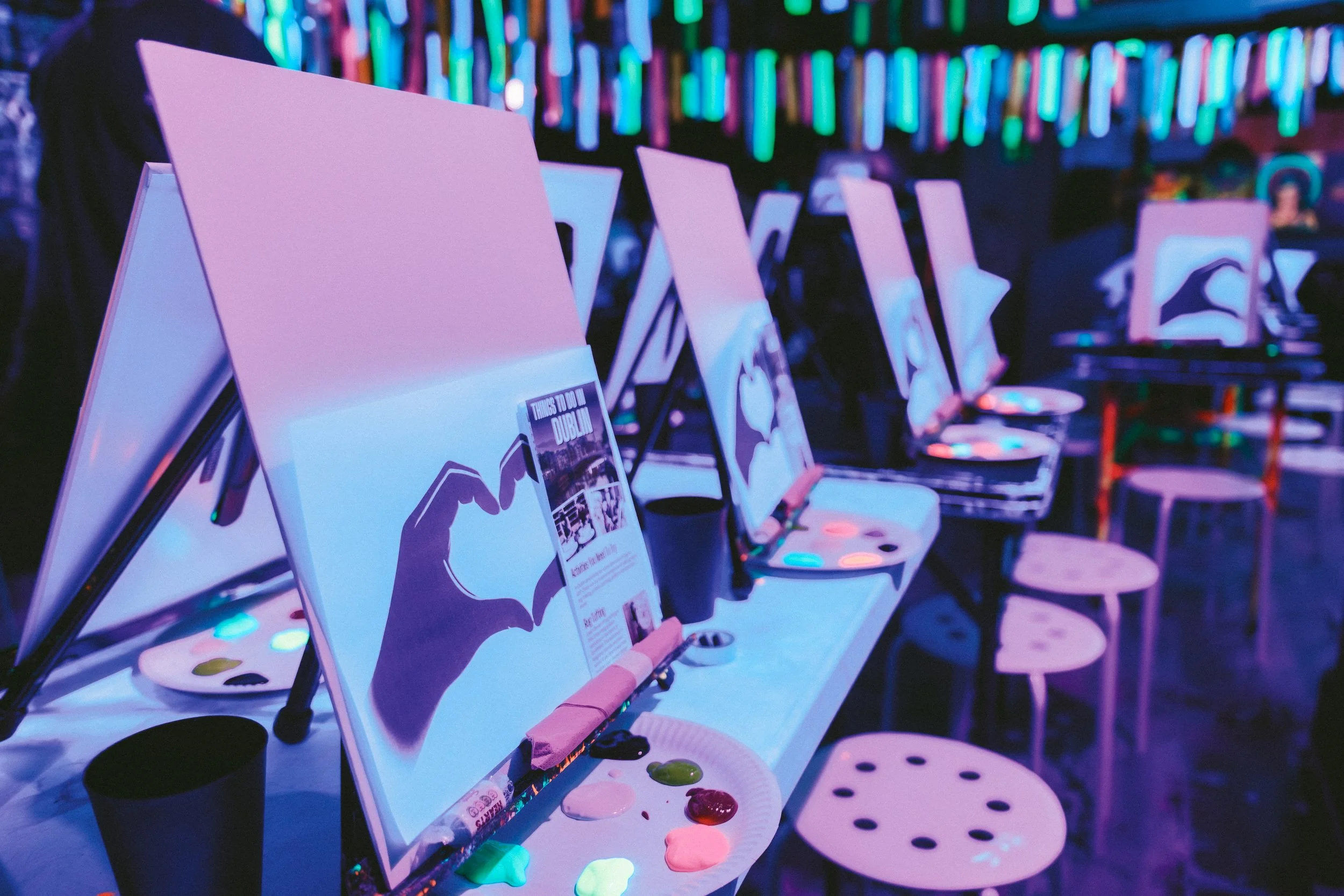 A group of people painting canvases in a neon themed-bar.