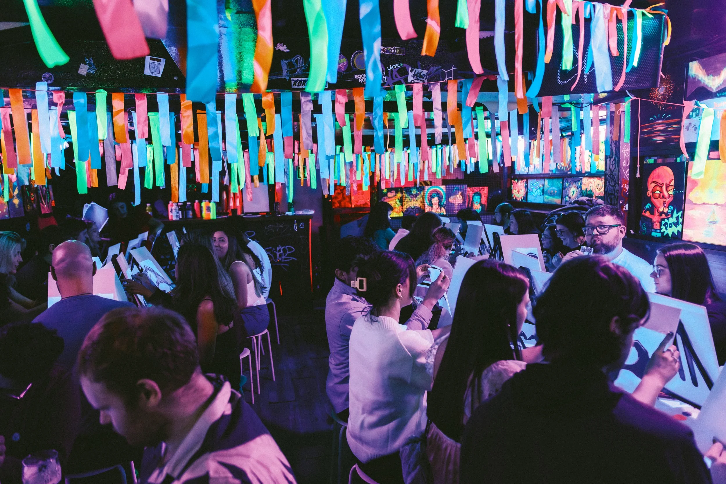 A man showing a pint of beer, while the people keeps painting at the background.
