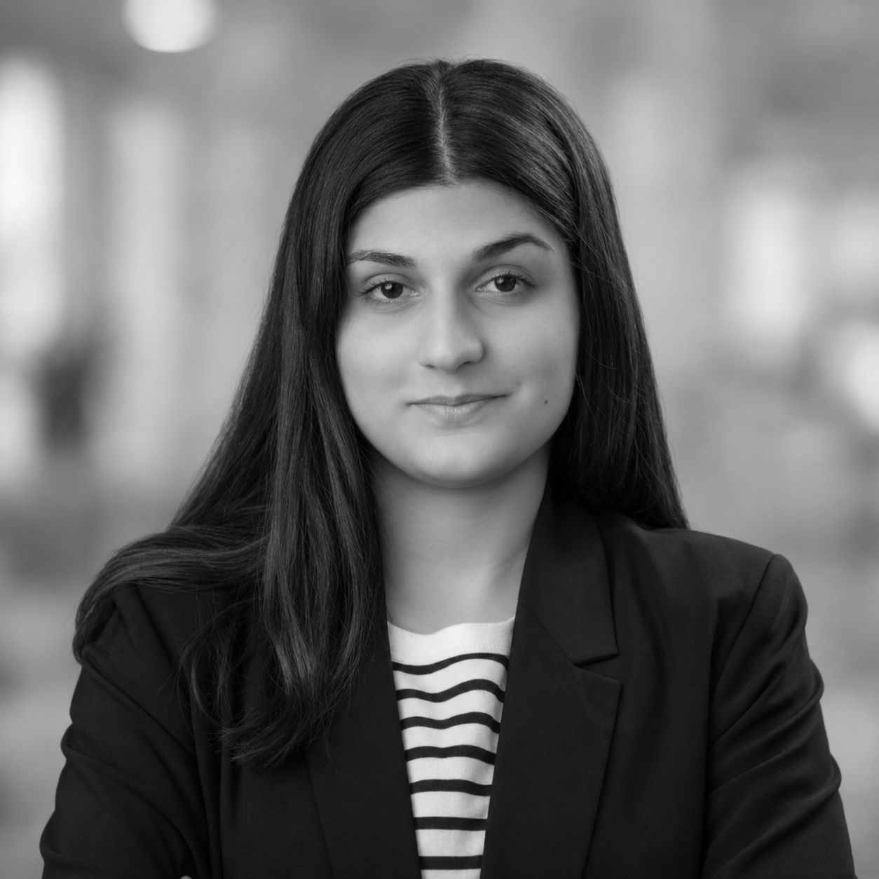 Black and white portrait of a woman with long dark hair, wearing a blazer over a striped shirt, looking directly at the camera with a slight smile.