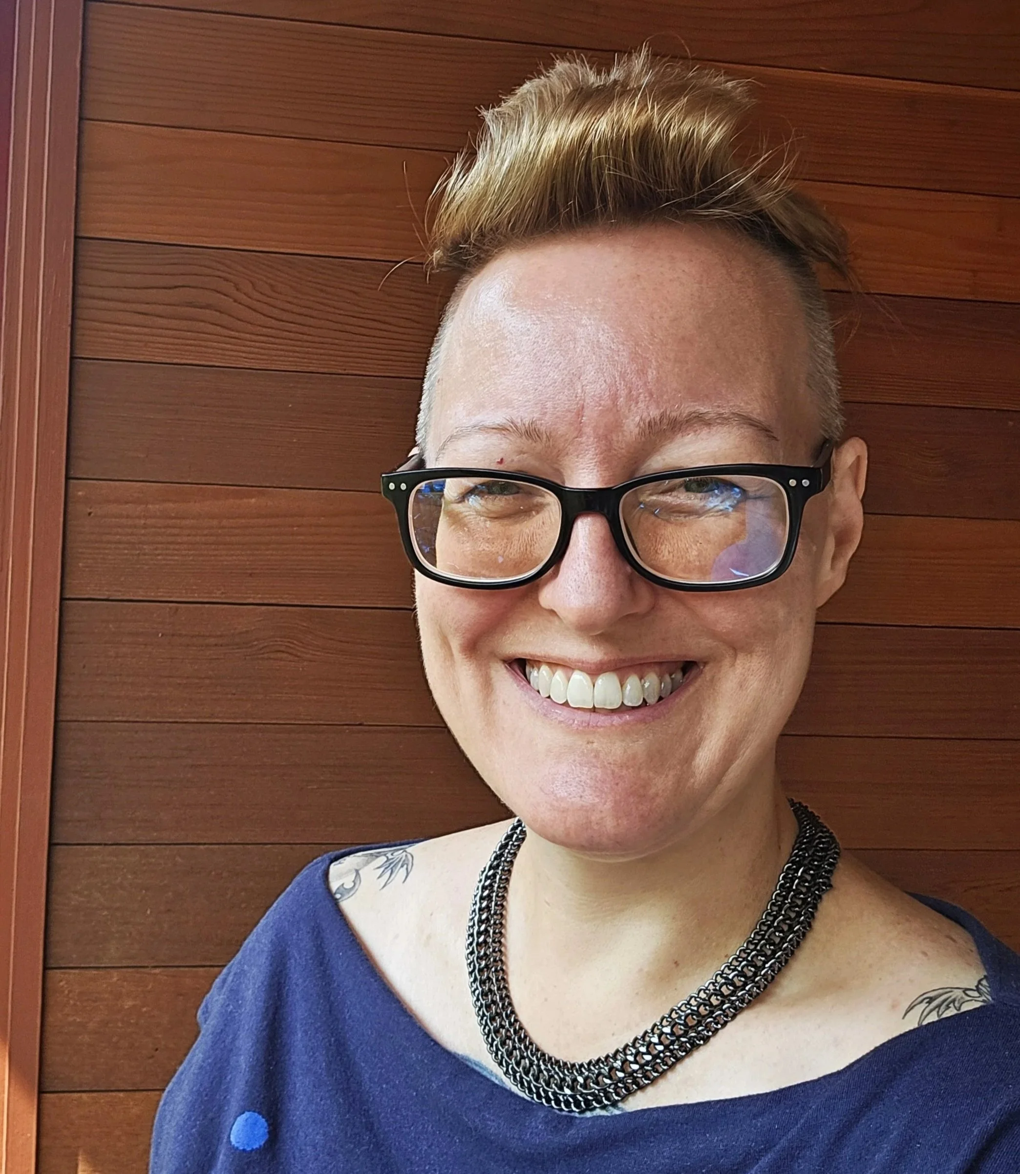 Face photo of registered clinical counsellor Melanie Armstrong, a white woman with short blonde hair wearing a blue shirt standing on a balcony.