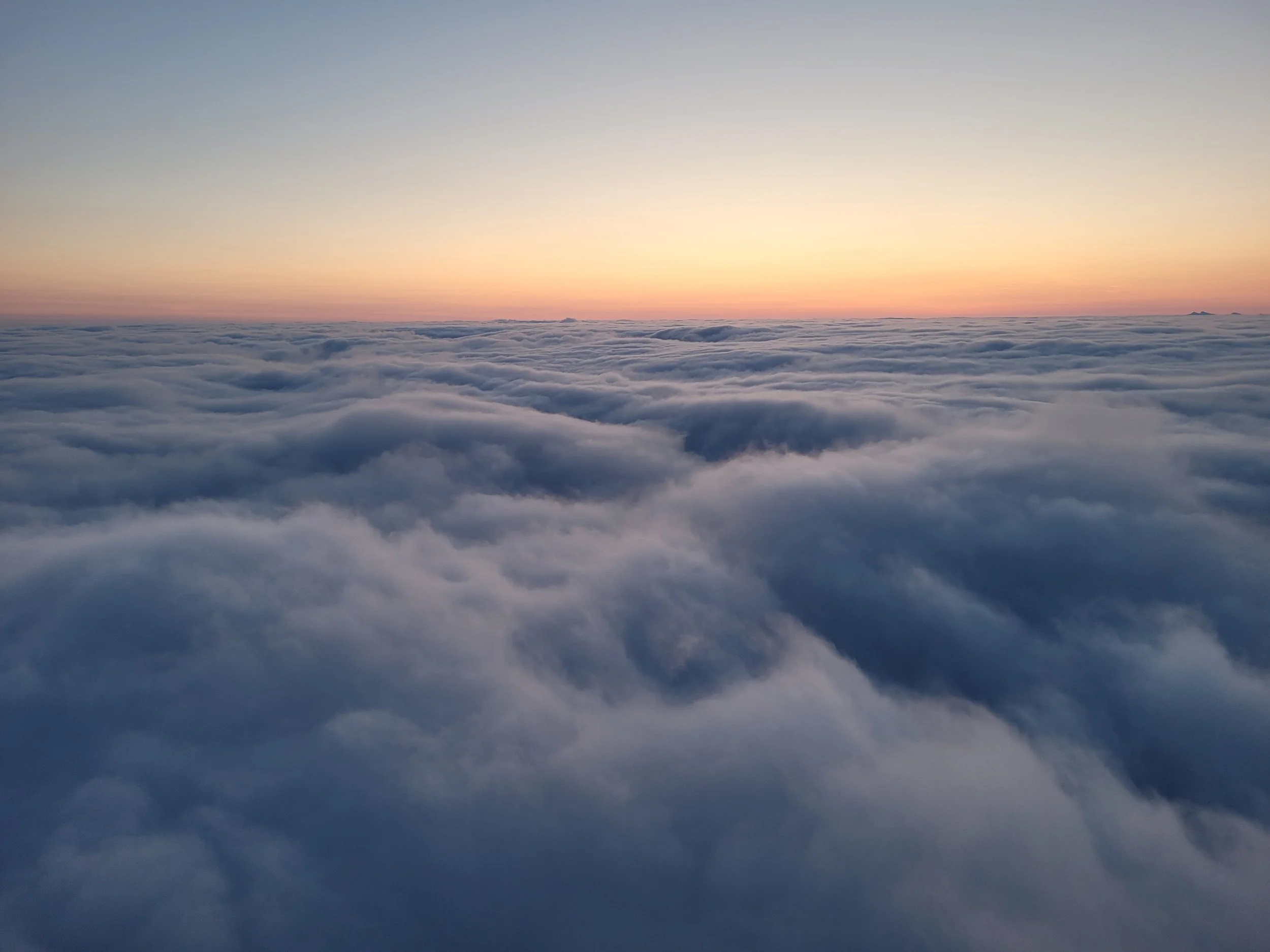 En utsikt over skyene ved solnedgang eller soloppgang, med en tydelig horisont og noen små øyer i det fjerne.