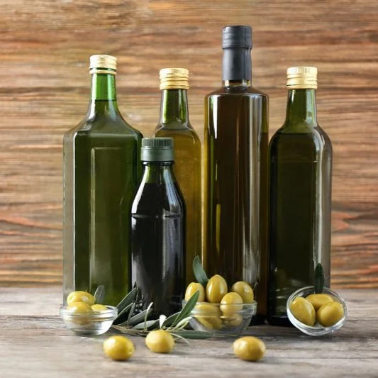 Various bottles of olive oil and bowls of green olives on a wooden surface.