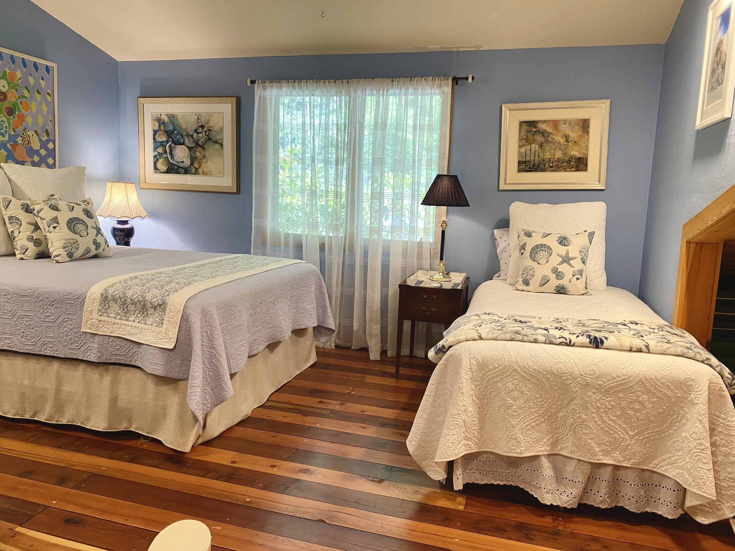 A bright and blue ocean themed bedroom, with multiple beds and sunny windows.