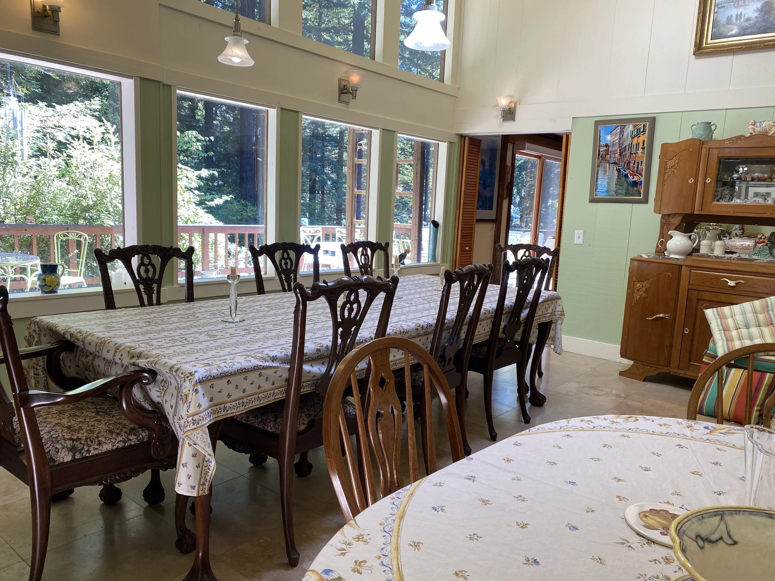 Dining room with sage green walls, antique wood chairs, and floral tablecloth.
