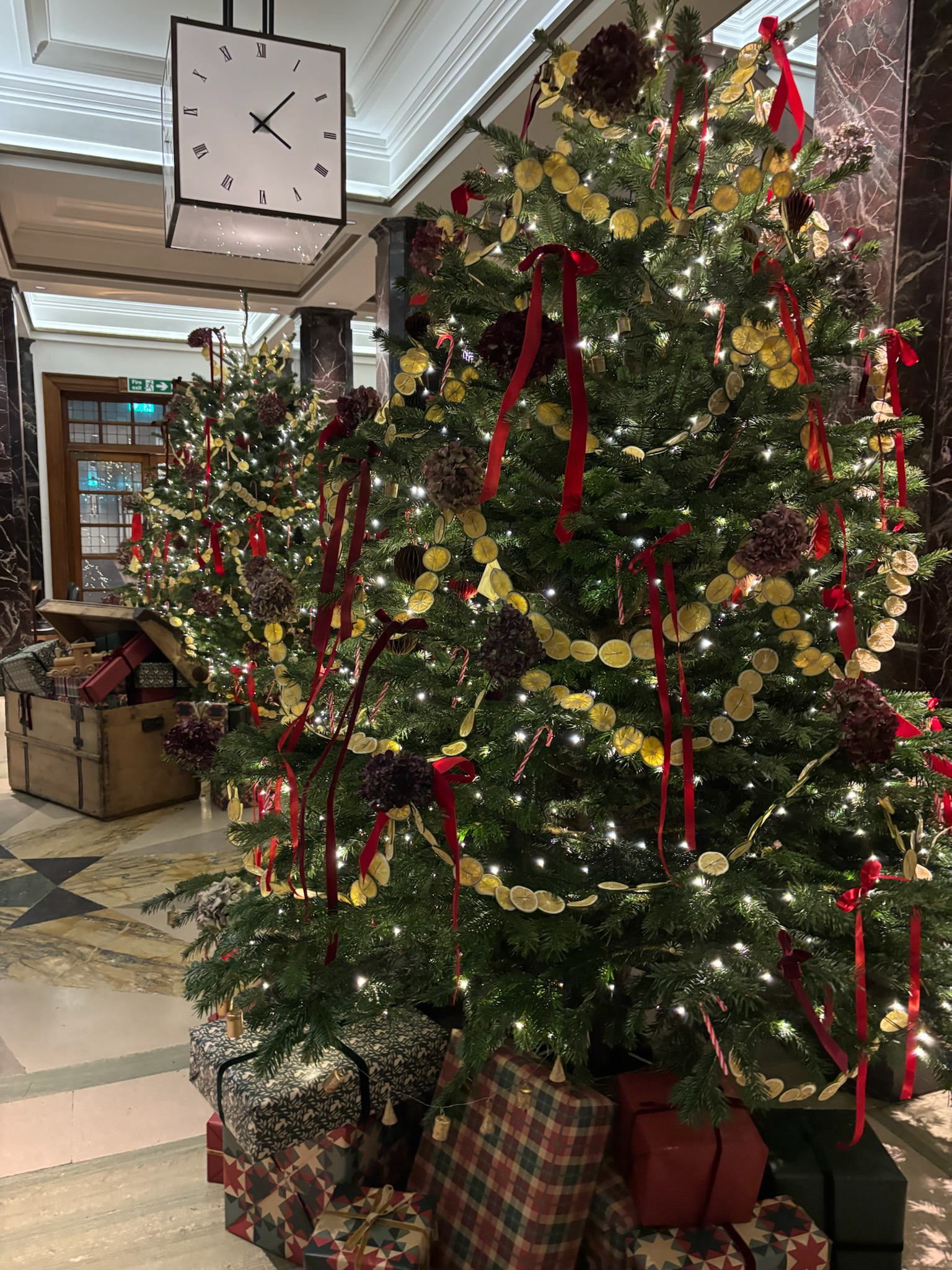 Decorated Christmas tree with red ribbons, dried lemon slices, and purple hydrangeas, with wrapped presents underneath in an elegant indoor setting.