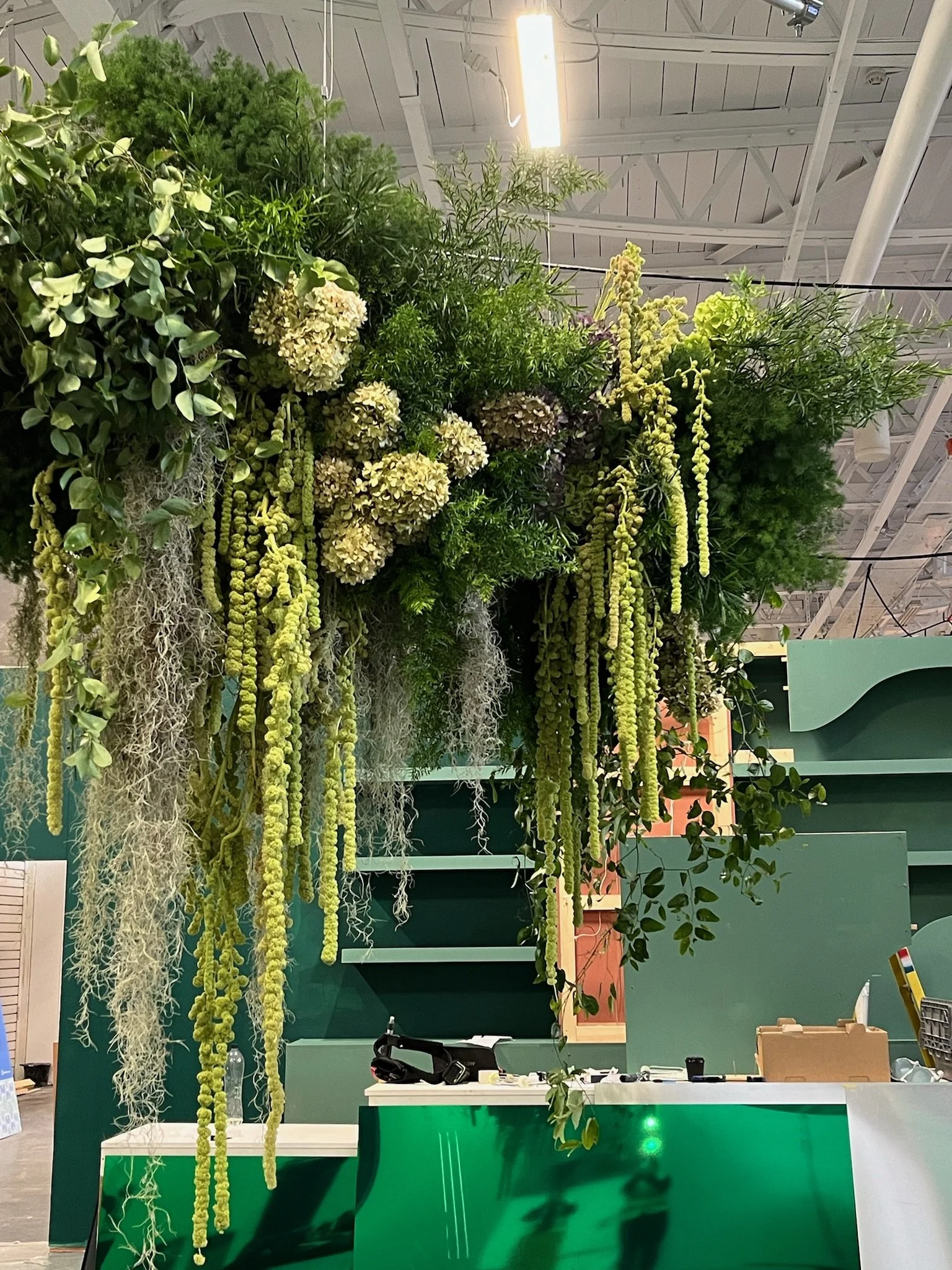 A floral arrangement with hanging green and white flowers and foliage above a green counter in a retail store.