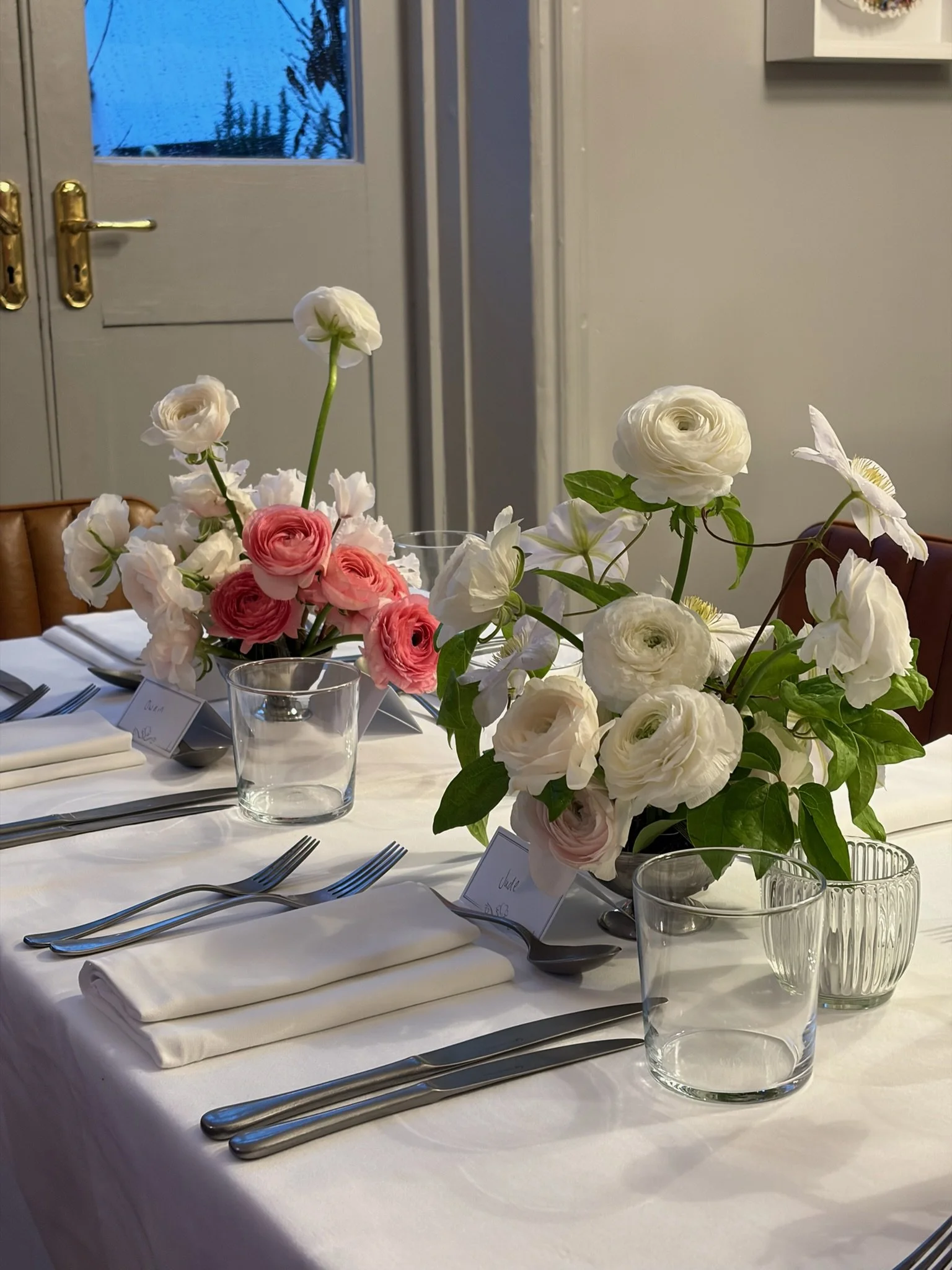 Table set for a formal event with white tablecloth, silverware, white napkins, and floral centerpieces with white and pink flowers in glass vases.