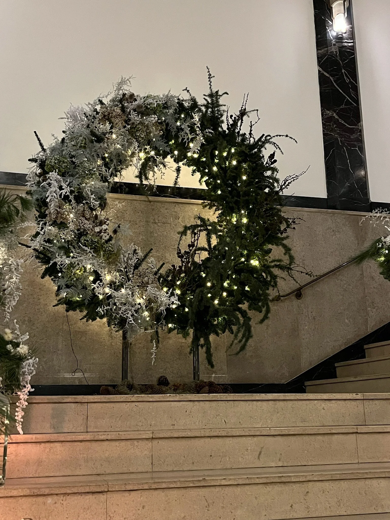 Decorative Christmas wreath with white flowers, greenery, and small lights on a staircase balustrade.