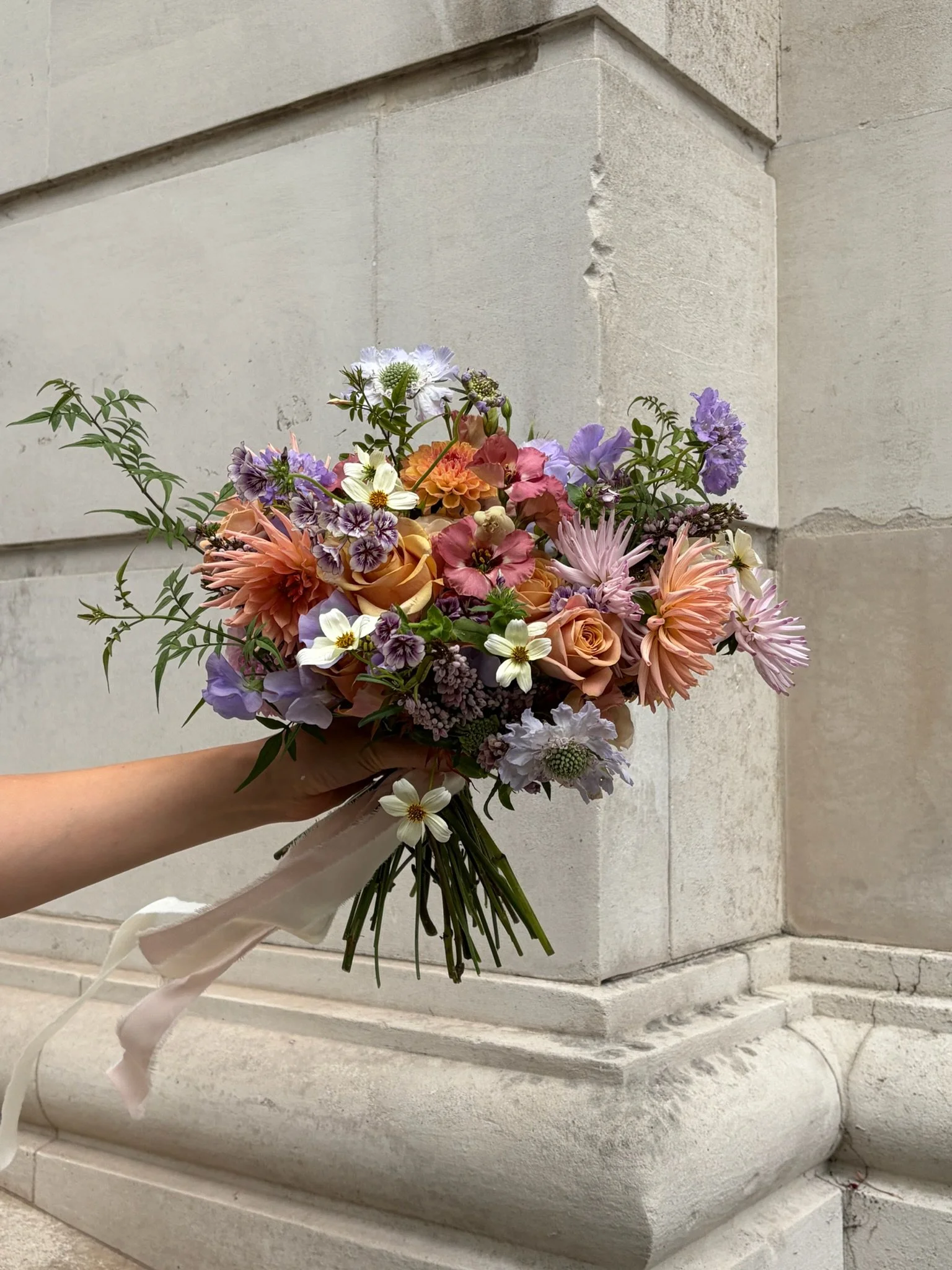 Person holding a colorful bouquet of flowers against a stone wall background.