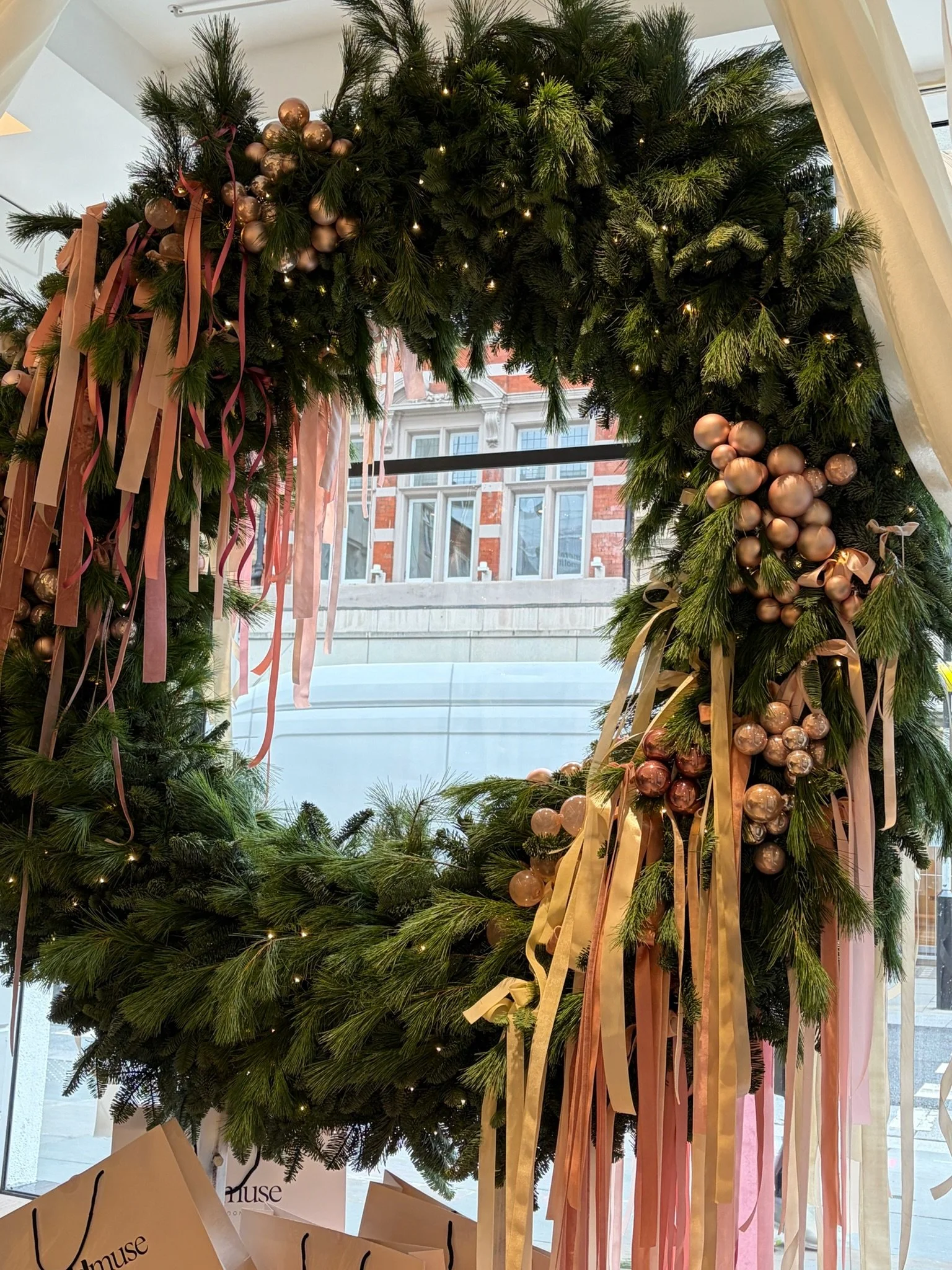 Decorative Christmas wreath with pink and gold ornaments and ribbons hanging in front of a window