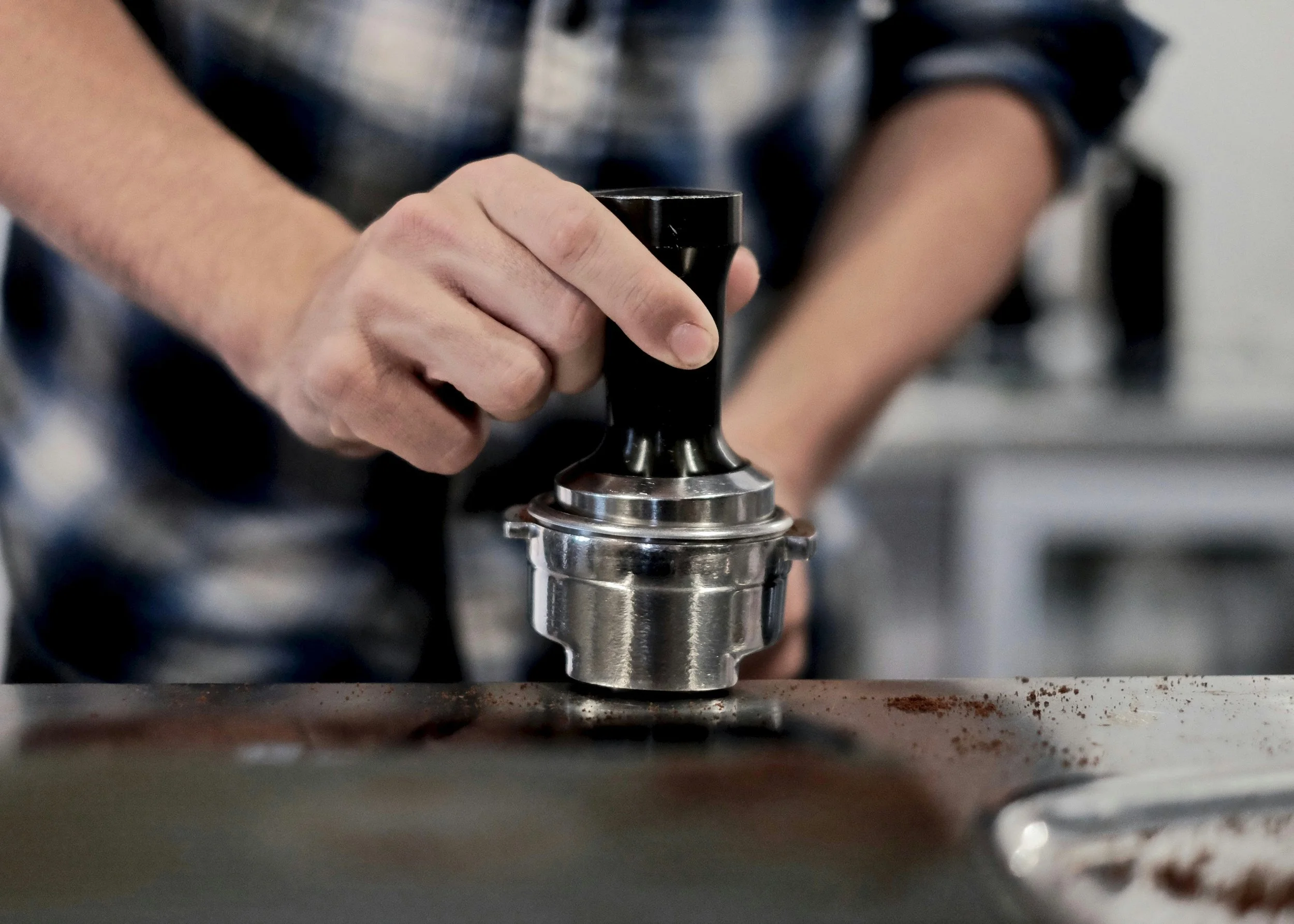 A person is using a metal crank handle to operate a machine, with coffee grounds scattered on the surface below.