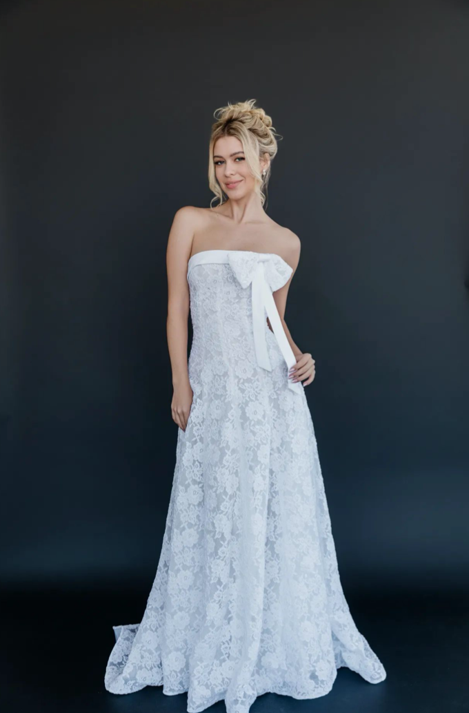 Gown "Daffodil" is crafted from stunning corded floral lace, delicate organza, and soft satin bridal lining. Featuring a detachable bow detail, its fitted bodice gently transitions into a flowing skirt, creating a look that is both sweet and distinct