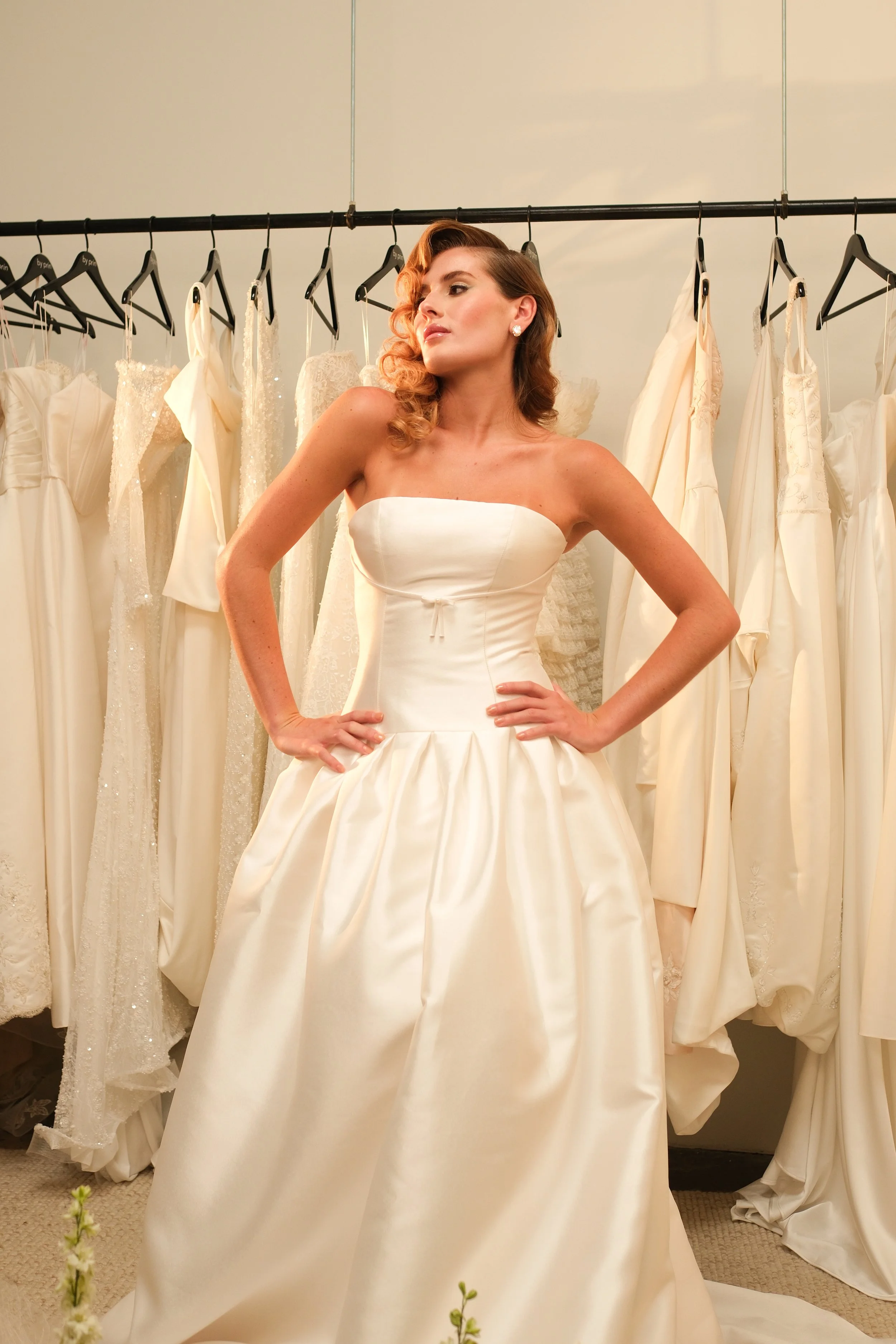 The 'Monroe' gown features elegant pleating at the hips, a flattering drop-waist silhouette, and a delicate bow just below the bust. Feminine and sophisticated, this gown exudes a timeless yet effortlessly chic charm.