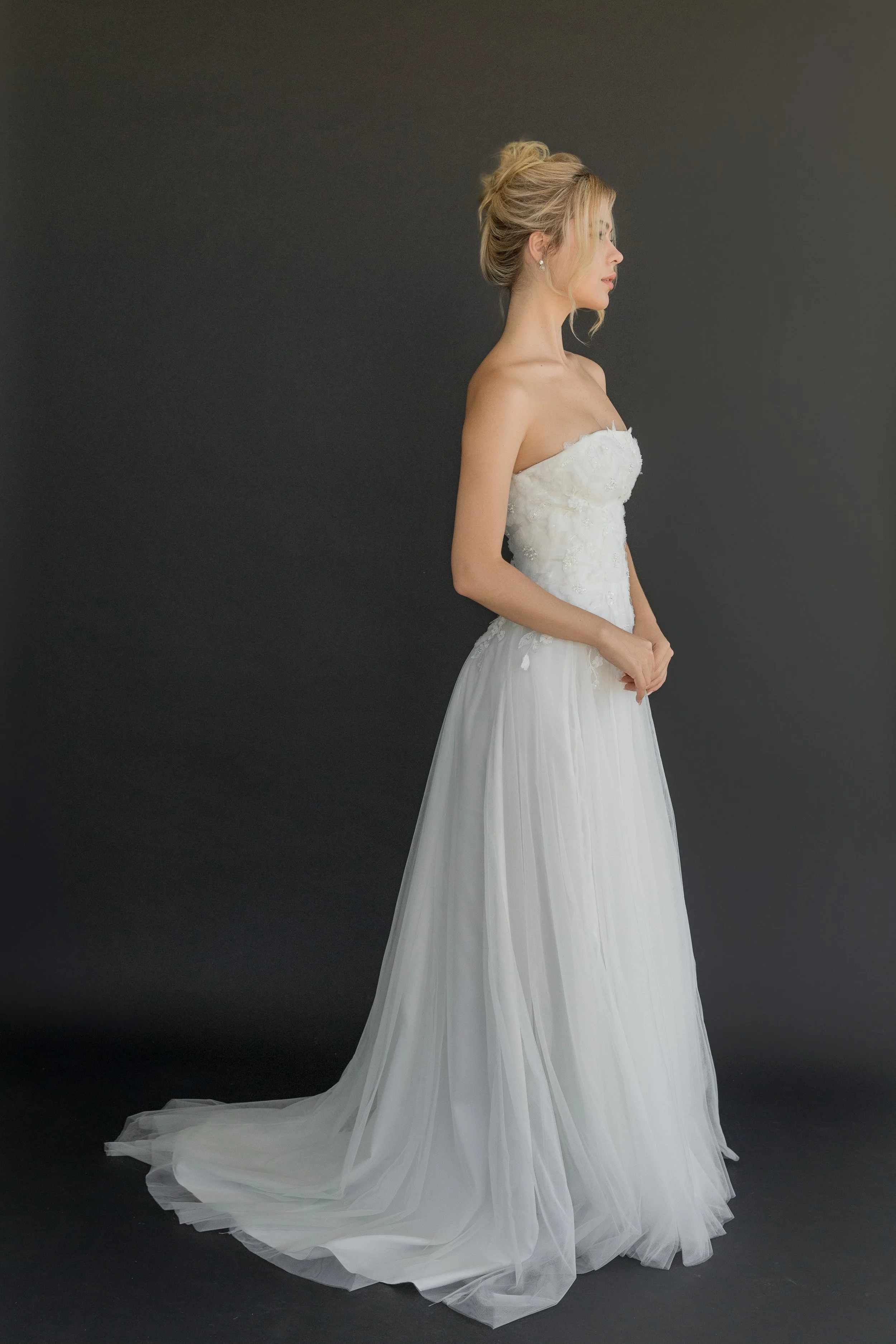 Gown "Monarch" features a delicate beaded tulle with floral feather appliqué, offering a look that is both unique and timeless. This lightweight, strapless gown is perfect for the bride seeking a minimalist yet feminine aesthetic. Effortlessly comfor