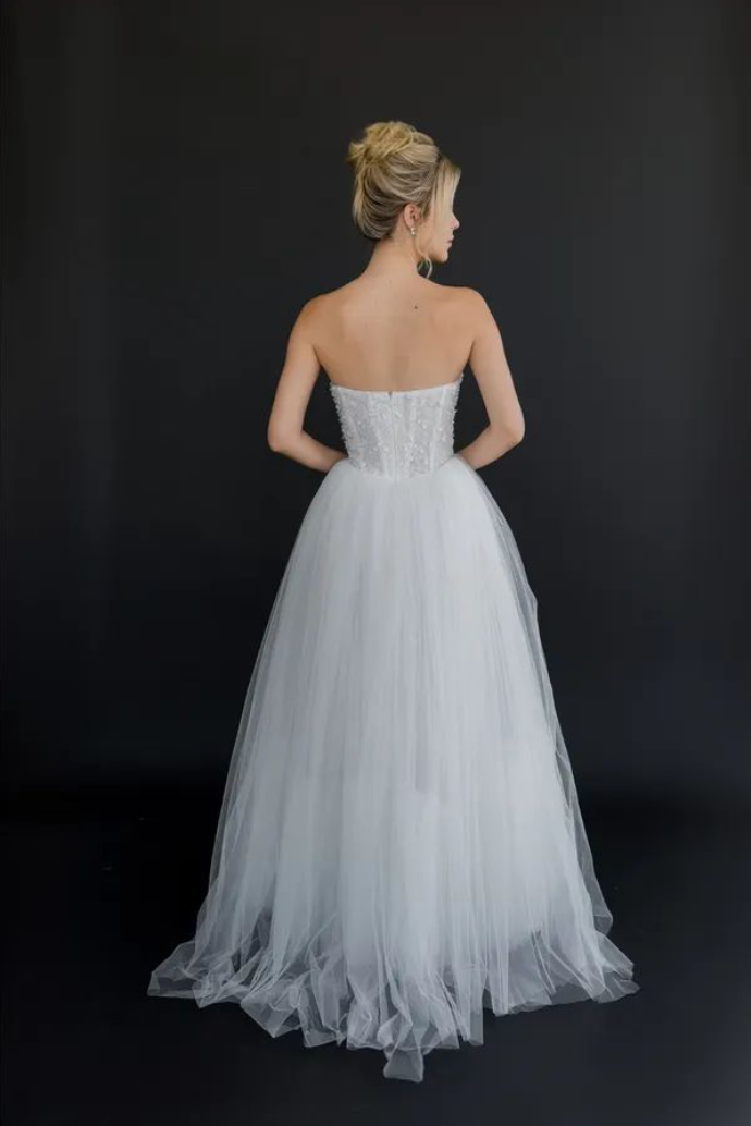 Gown "Nimbus" is crafted from intricately beaded embellished fabric, layered with soft organza and airy tulle. Featuring a flattering waistline and a structured, boned bodice, this gown beautifully blends a fairytale silhouette with contemporary eleg