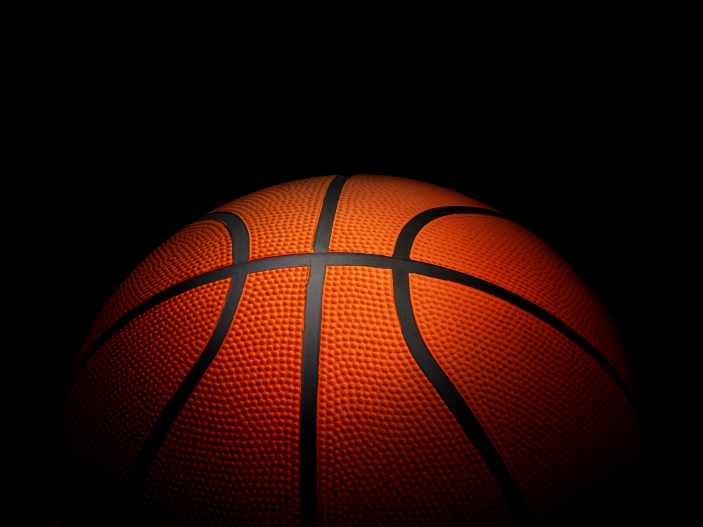 A close-up of an orange basketball with black lines, illuminated against a dark background.