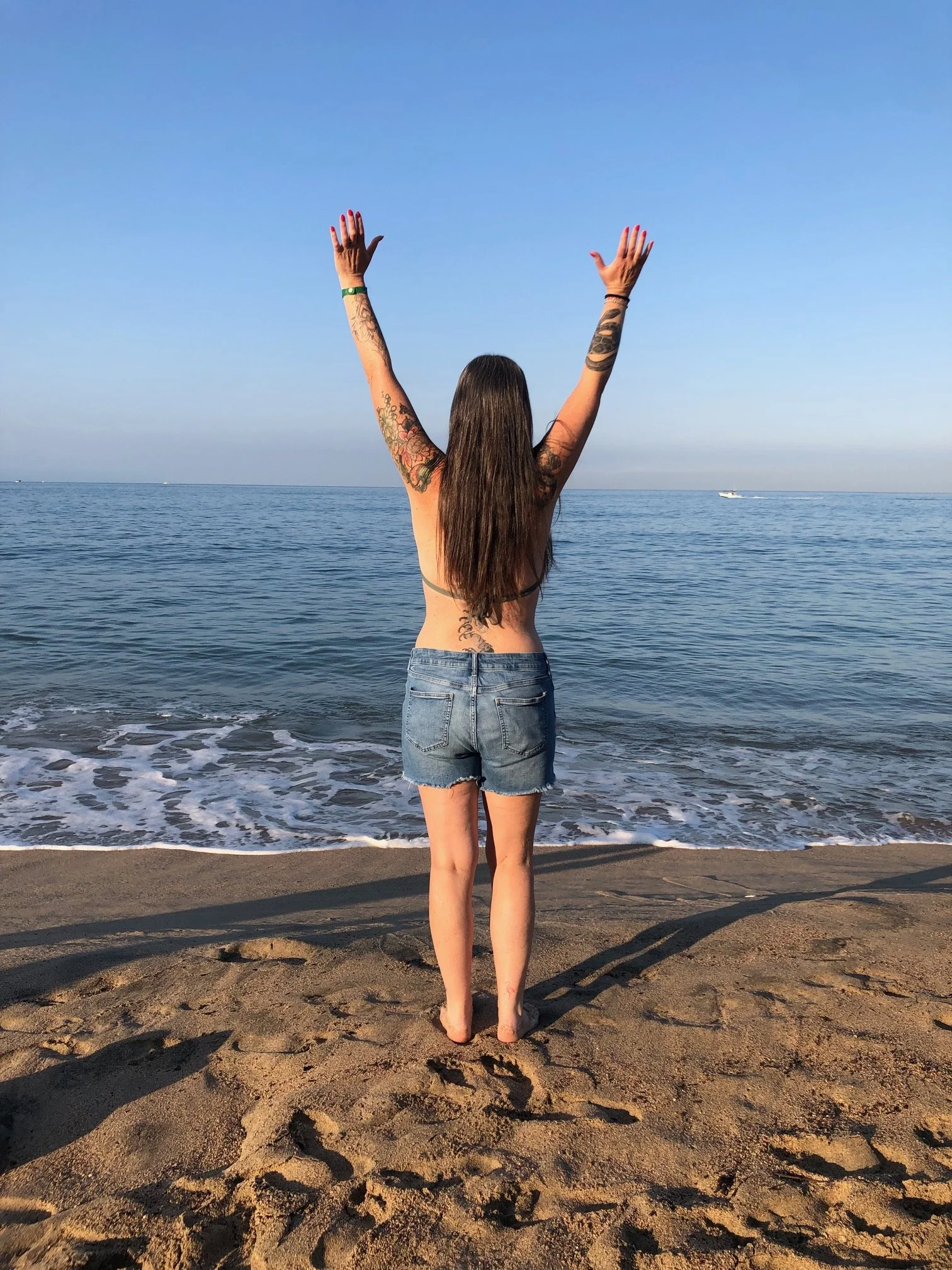 An adult stretching with arms raised with the ocean lapping gently at the sand beach at their feet