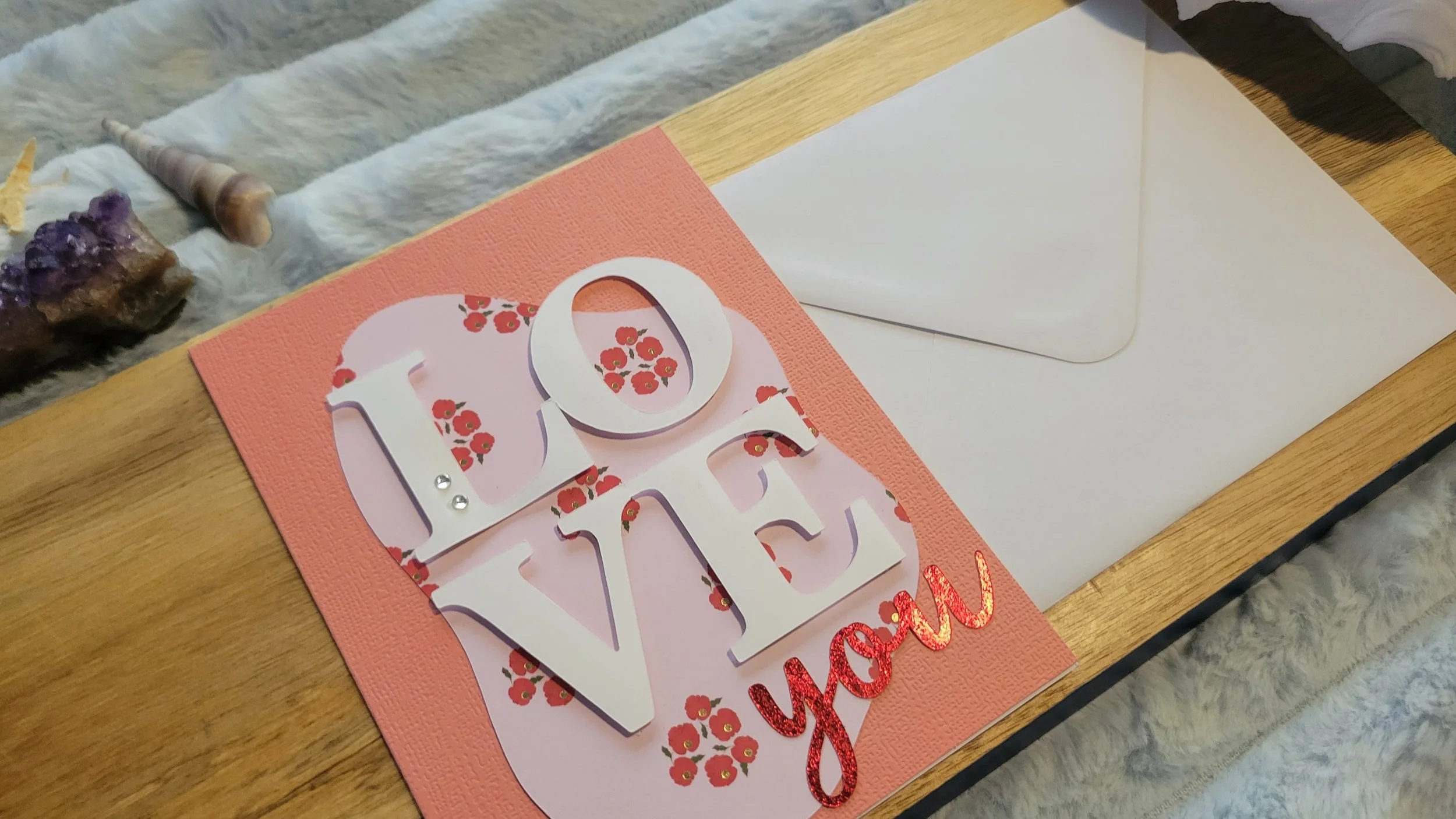 Pink handmade card with a pale pink and red poppy-patterned abstract shape, layered white “LOVE” lettering, and shiny red script “you” at the bottom.