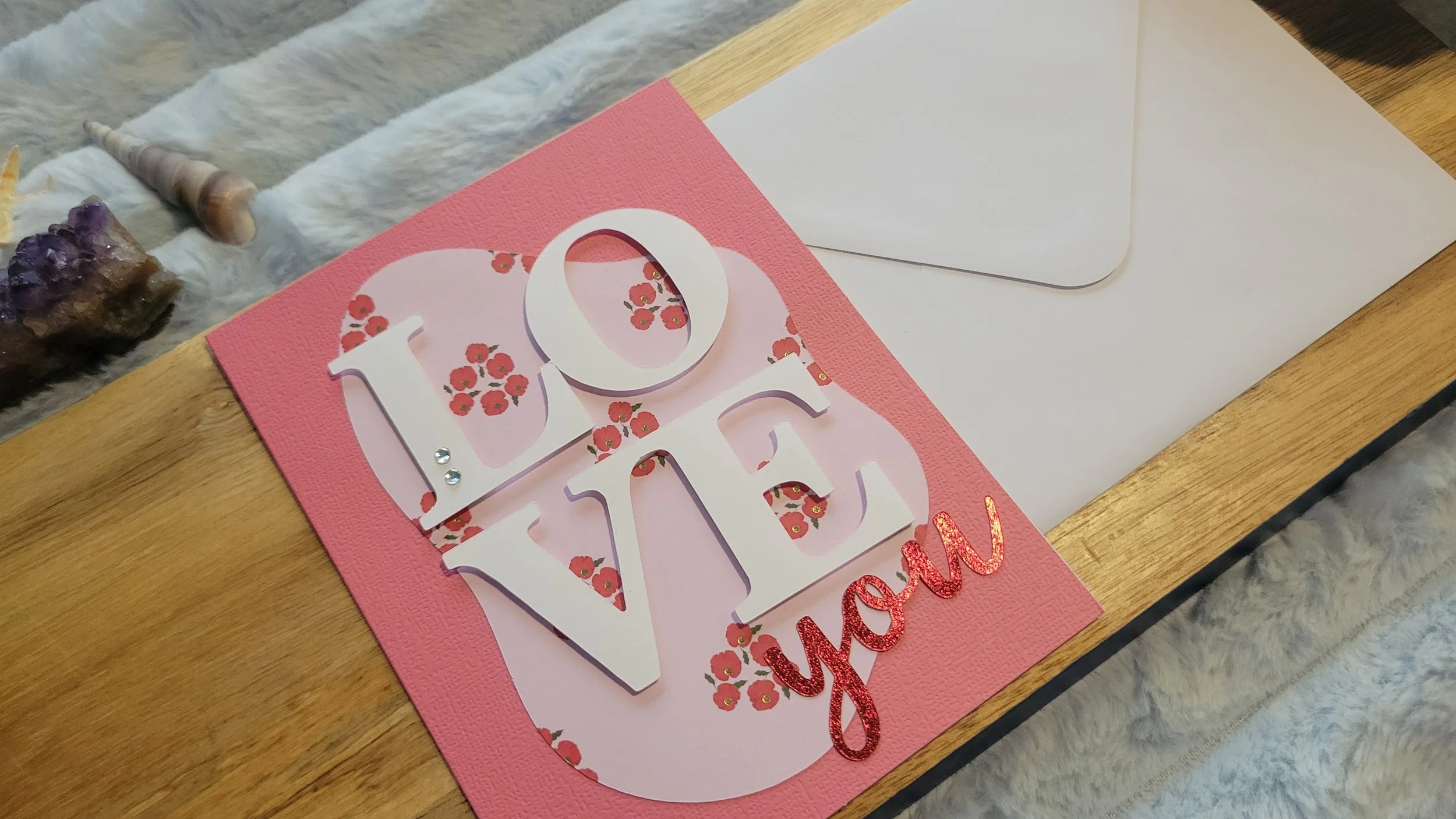 Pink handmade card with a pale pink and red poppy-patterned abstract shape, layered white “LOVE” lettering, and shiny red script “you” at the bottom.