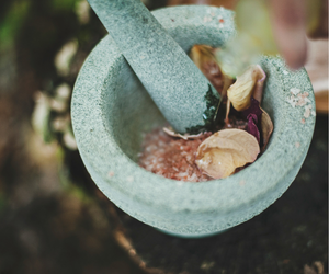 mortar and pestle with herbs and dried flowers for low-cost witchcraft and everyday ritual practices