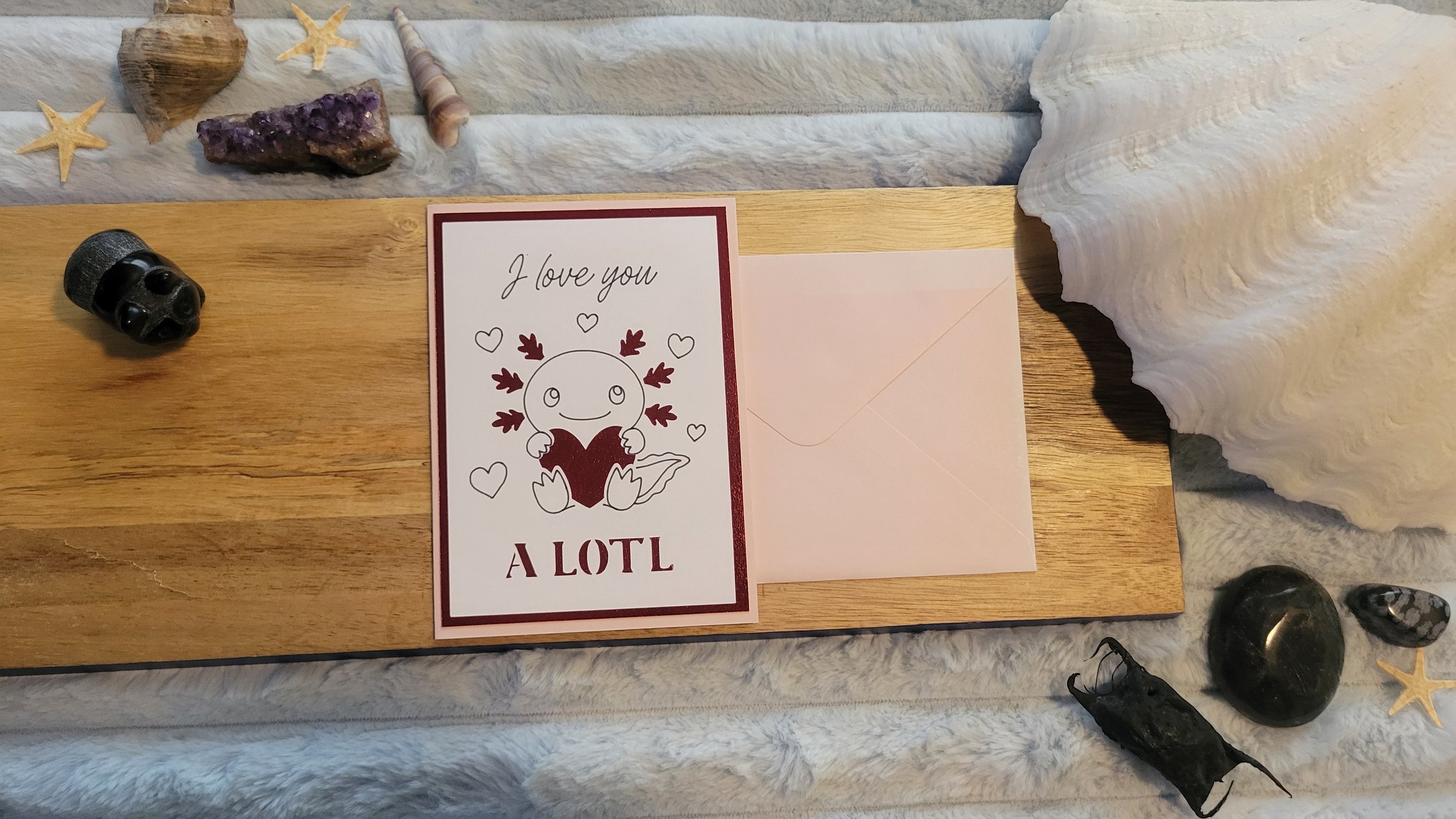 Handmade greeting card featuring a cute axolotl holding a heart with the phrase “I love you a lotl” and red metallic border accents.
