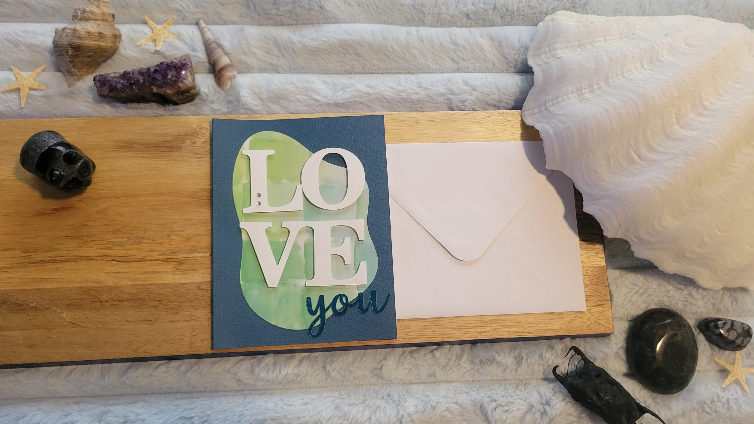 Navy handmade card with a blue-green watercolor abstract shape, layered white “LOVE” lettering, and shiny blue script “you” at the bottom.