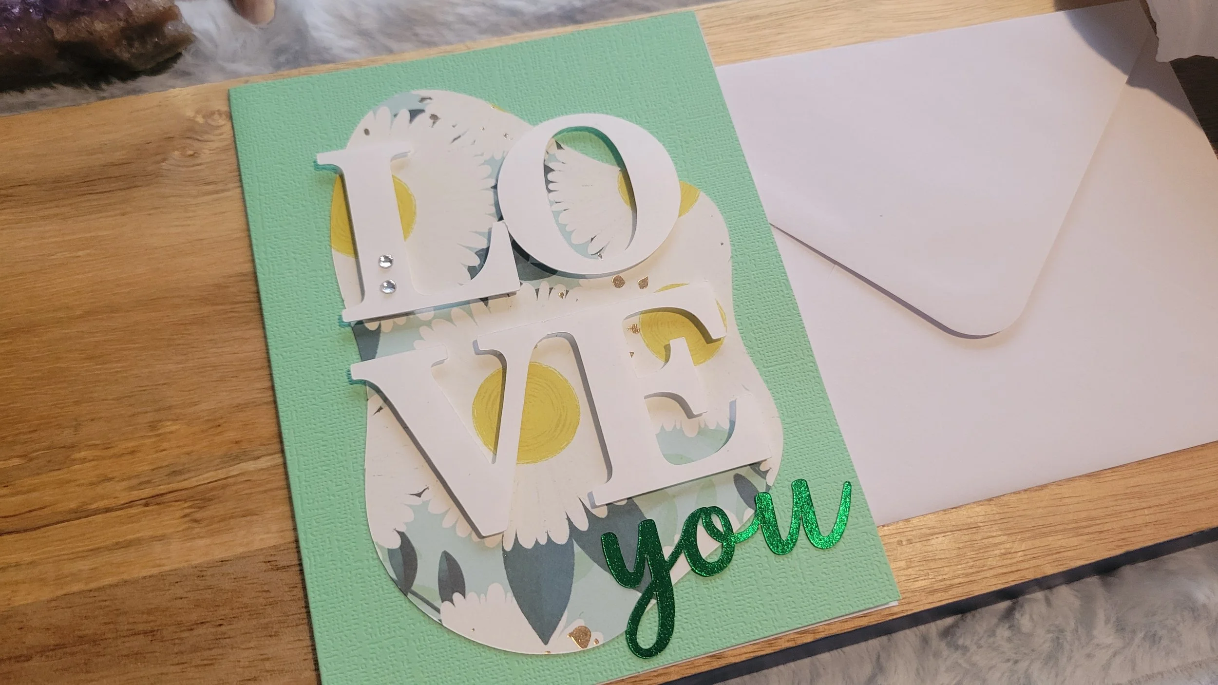 Light Green handmade card with a sunflower-patterned abstract shape, layered white “LOVE” lettering, and shiny green script “you” at the bottom