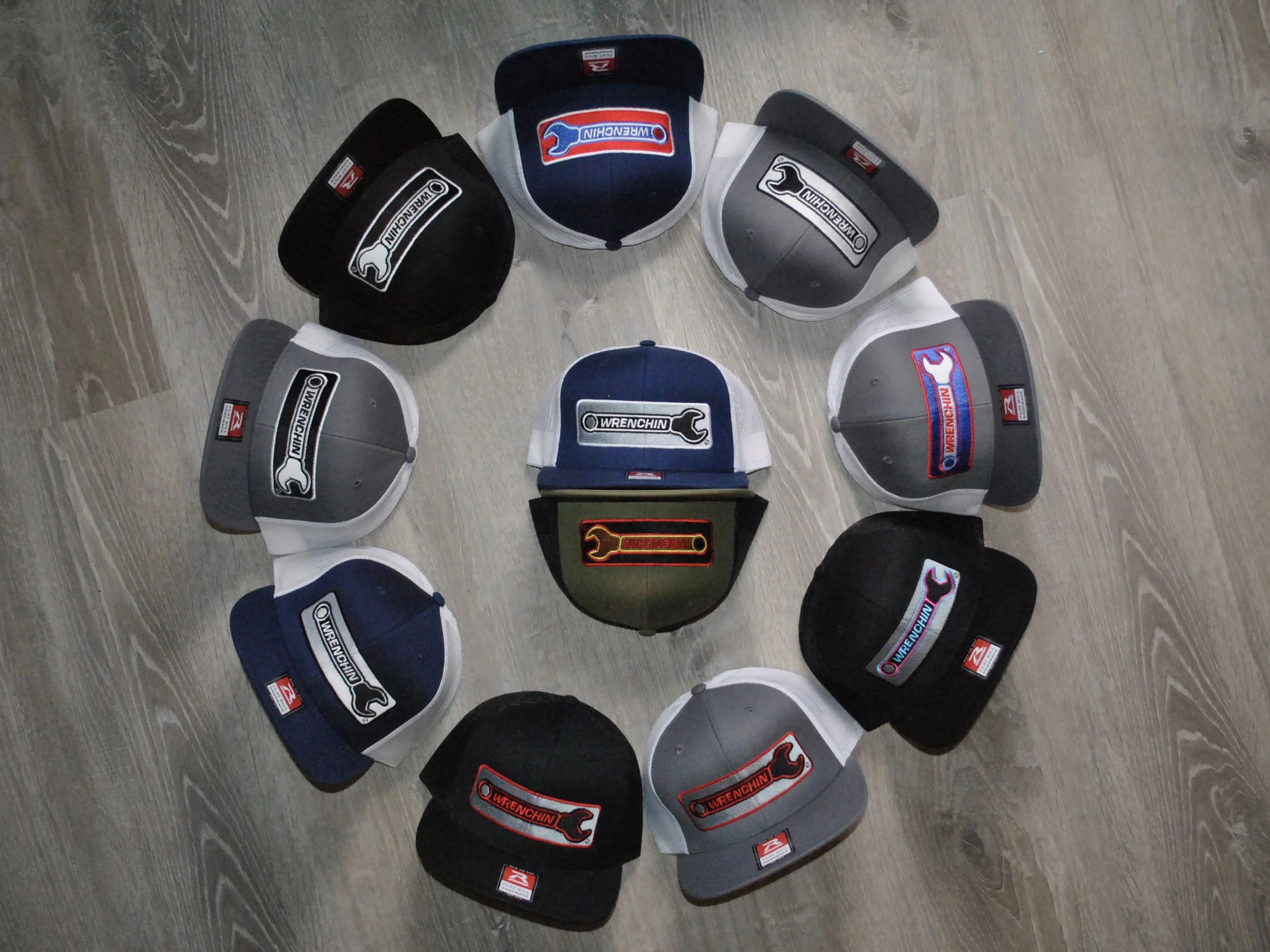 Collection of baseball caps with various brand logos arranged in a circle on a wooden floor.
