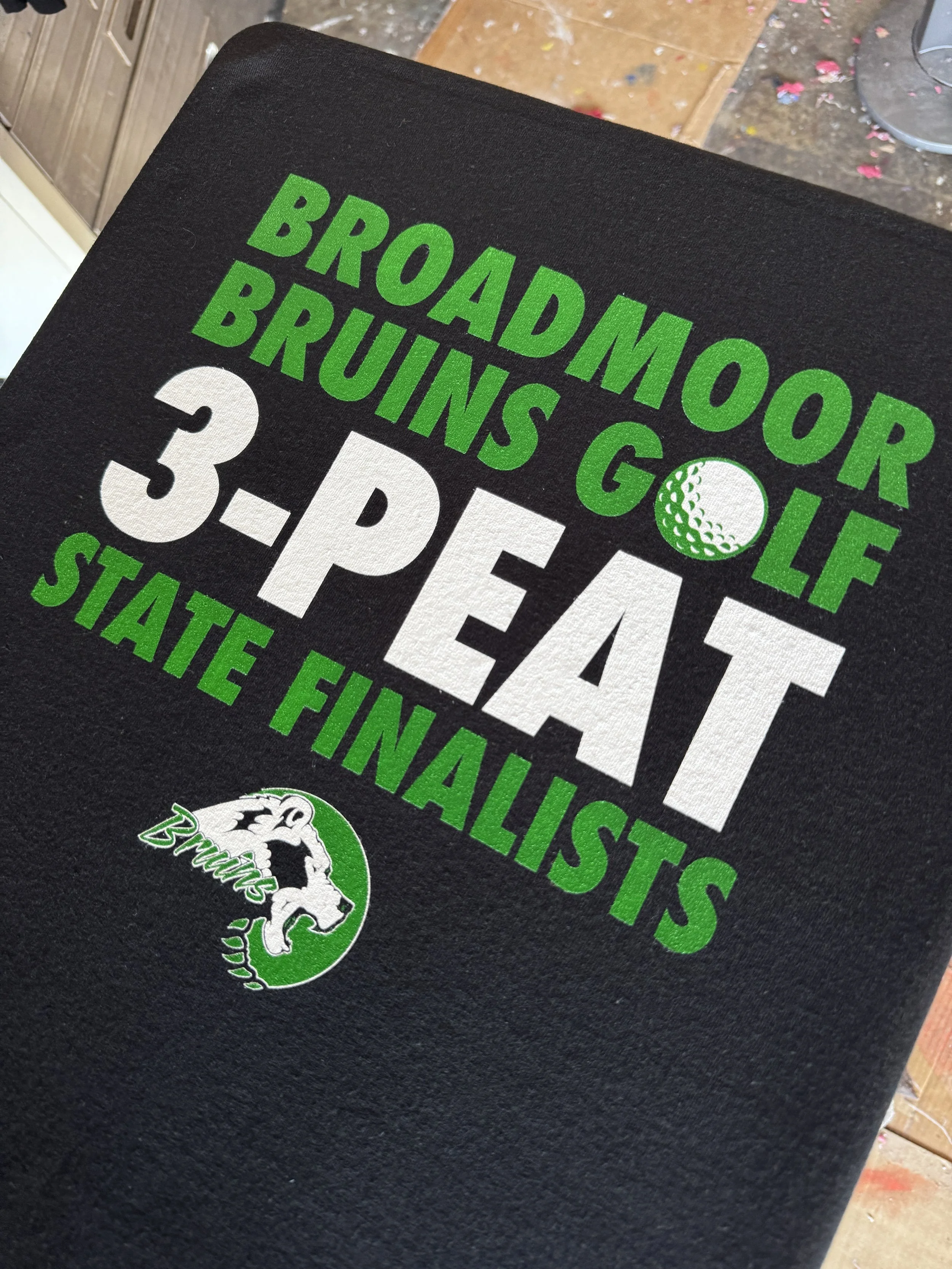 Black towel with green and white text celebrating Broadmoor Bruins golf team's third-place finish in the state finals.