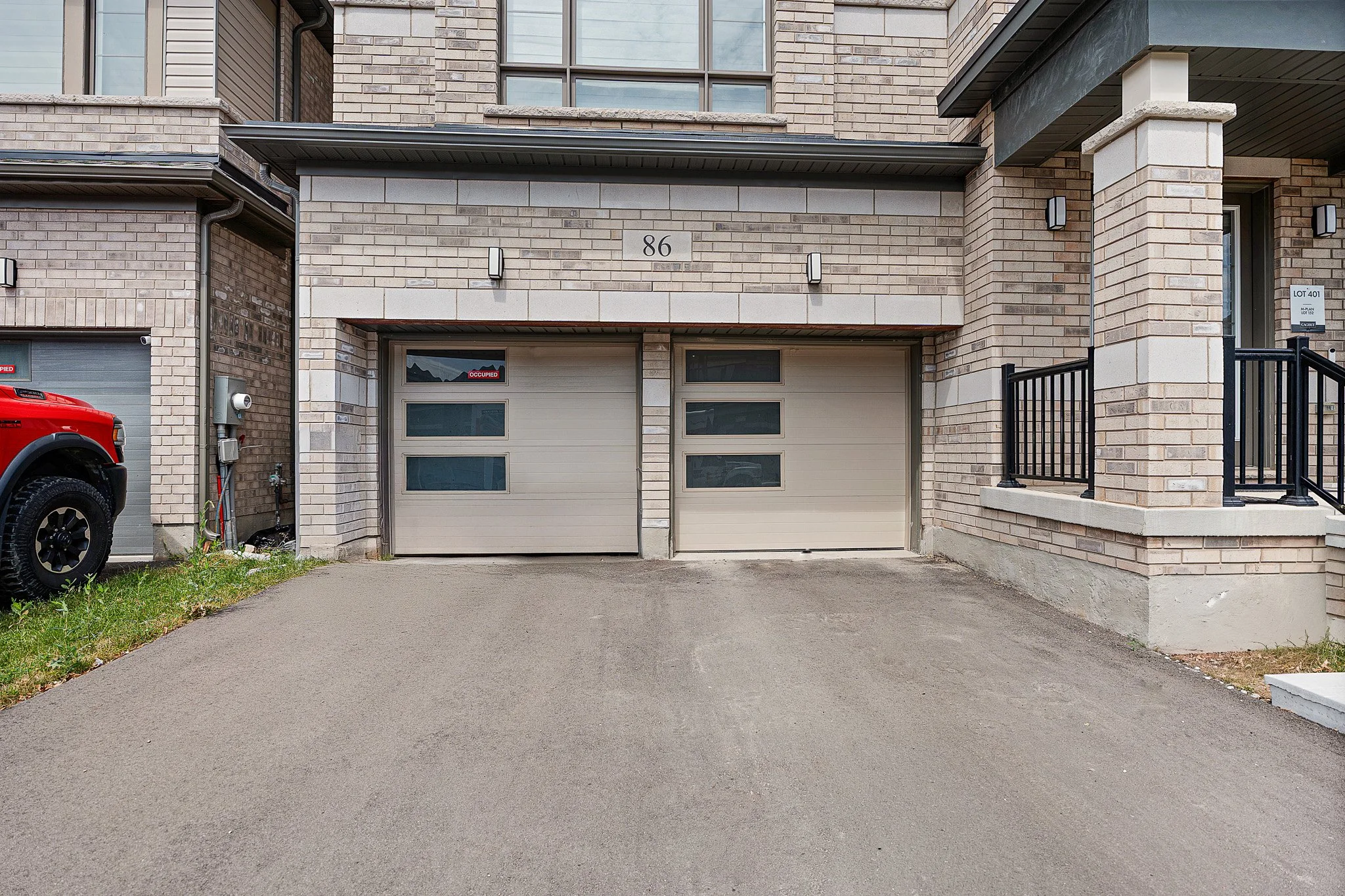 Front of a modern brick townhouse with two garage doors, one with an 'Occupied' sign, and a driveway.