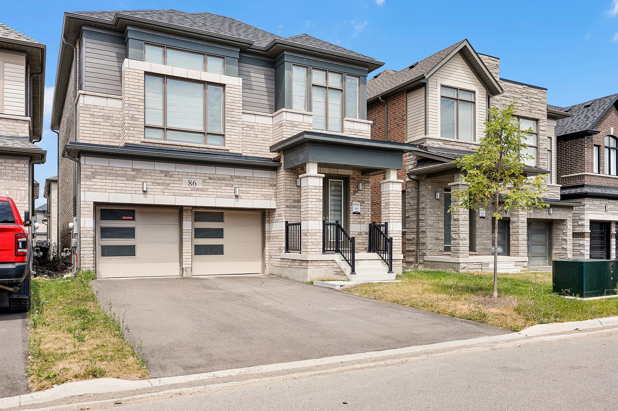 Front view of modern two-story townhouse with a garage, steps leading to the front door, and small tree in front yard.