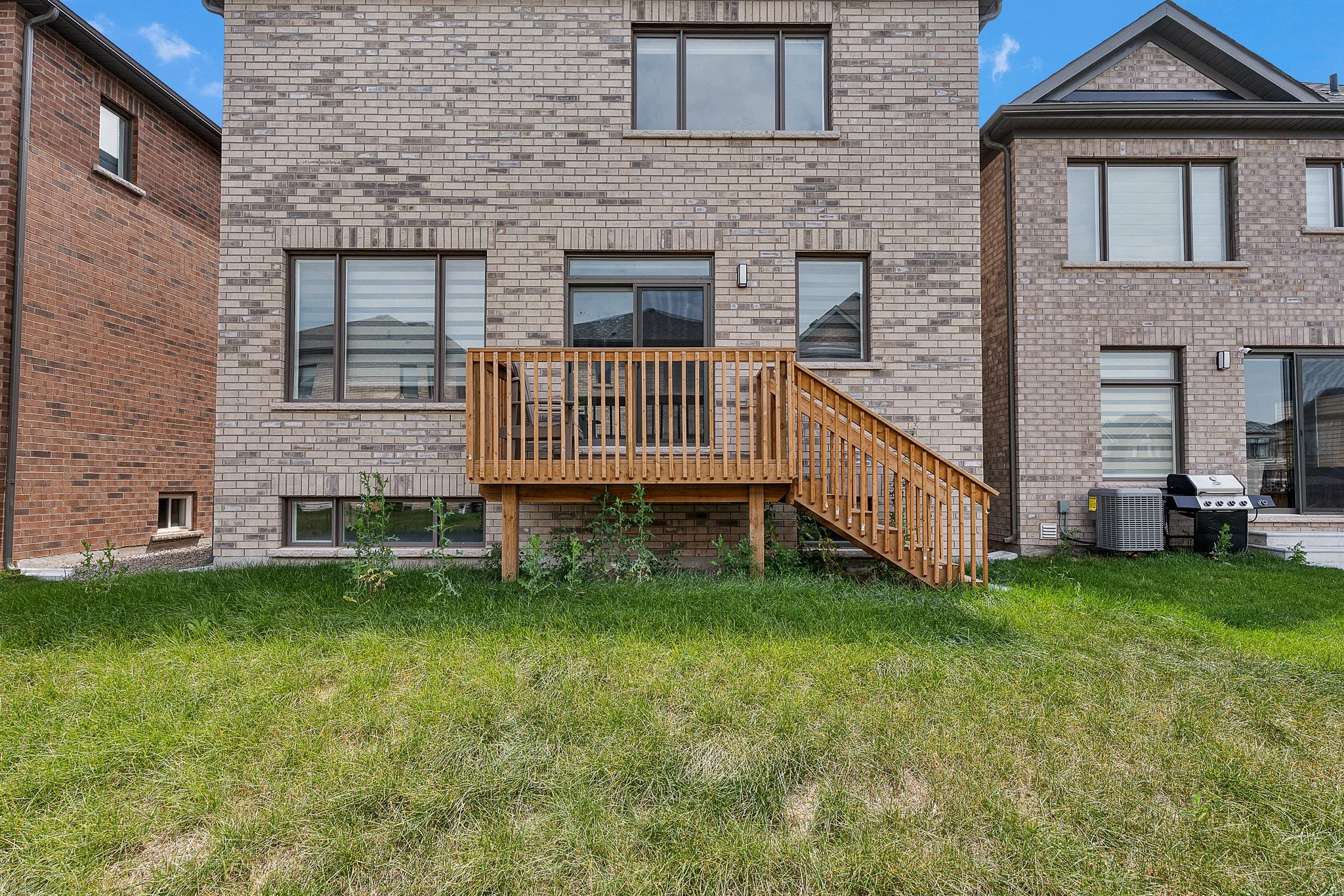 Backyard of a house with a small wooden deck, grass, and an air conditioning unit.