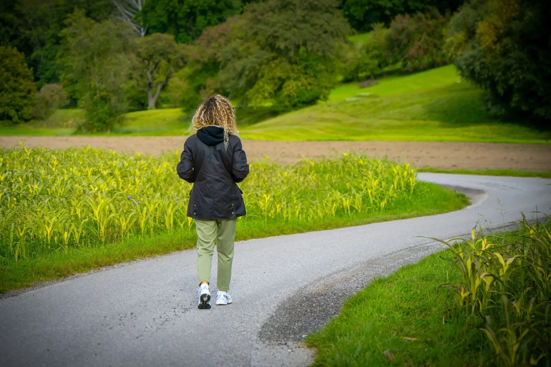 Woman walking alone on a winding path through green fields during a life transition, reflecting uncertainty and change.