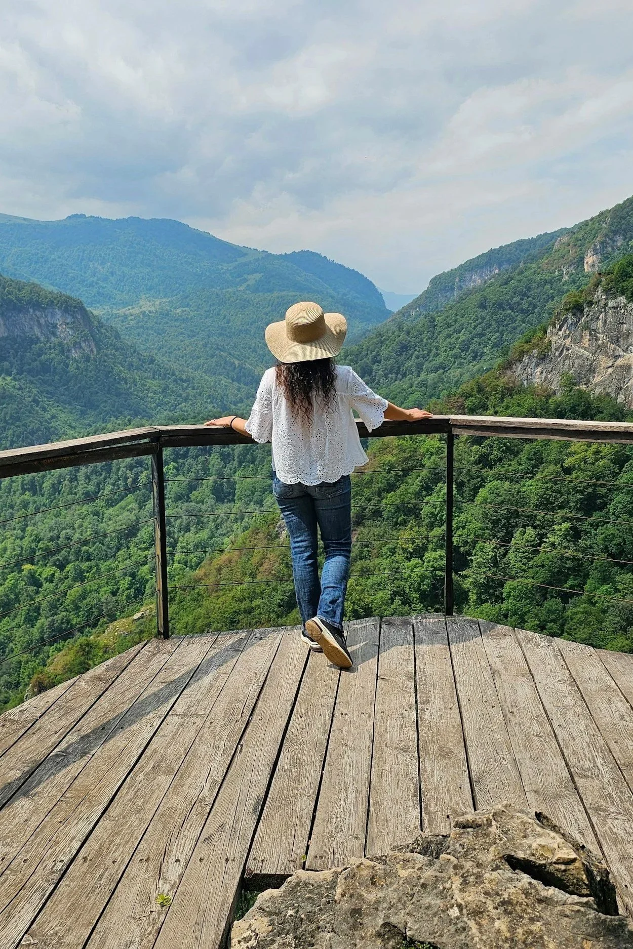 Woman in a sun hat looking out over a mountain vista from a wooden overlook