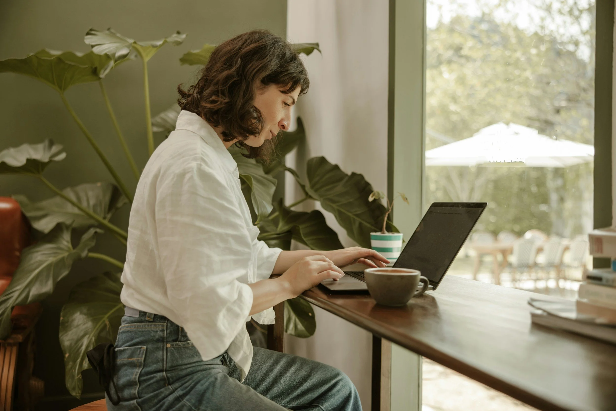 Woman using a laptop by a window with a cup of coffee