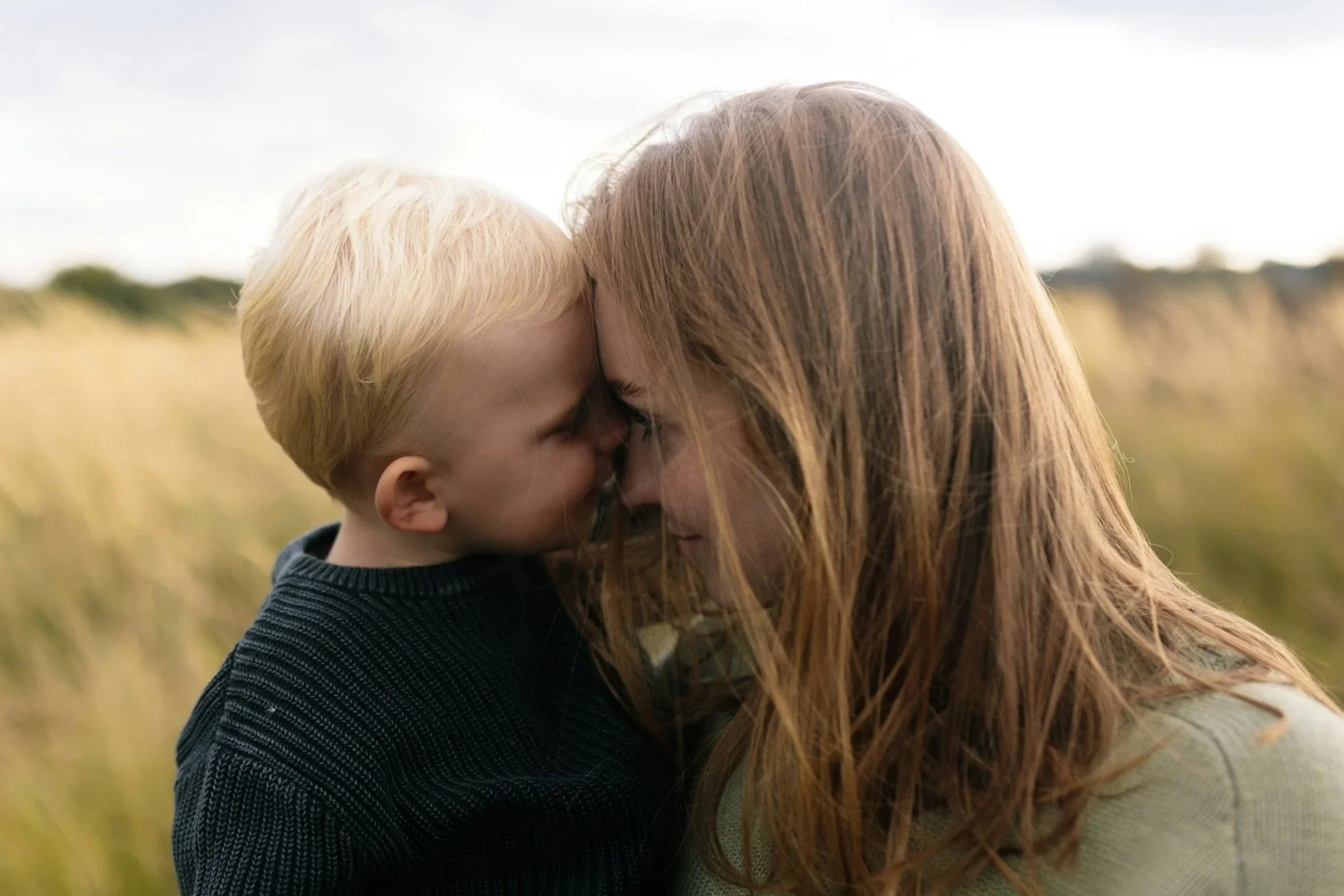 Mother and young son with foreheads touching in a grassy field