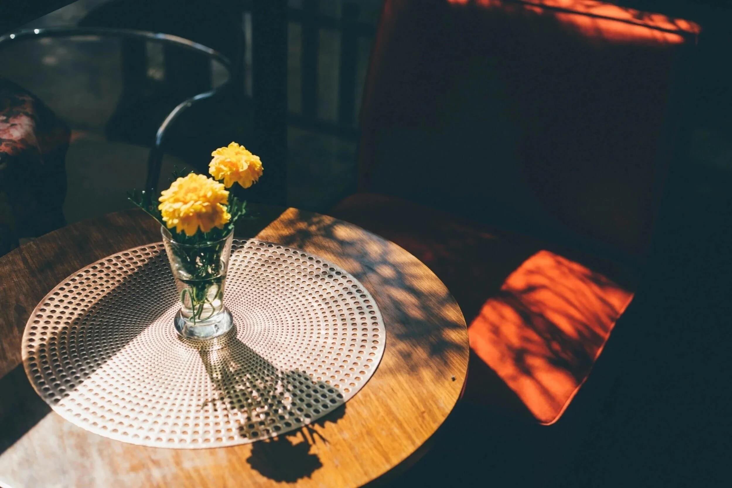 Sunlight falling across a small table with yellow flowers in a vase