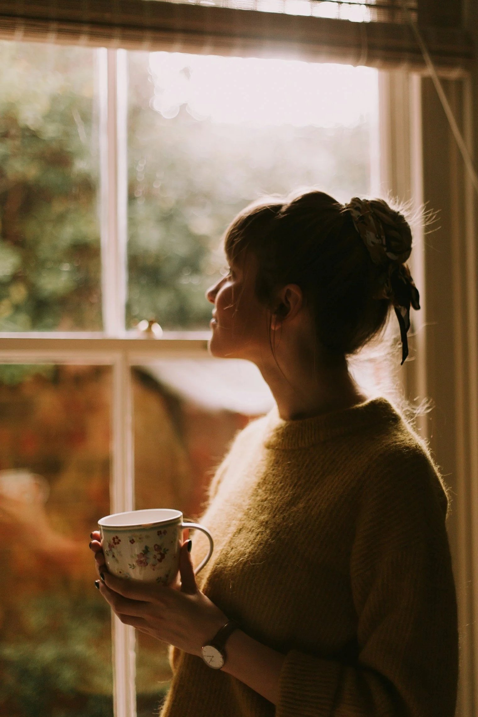 Woman with warm drink gazing out window – therapy for life transitions, reflection, calm support.