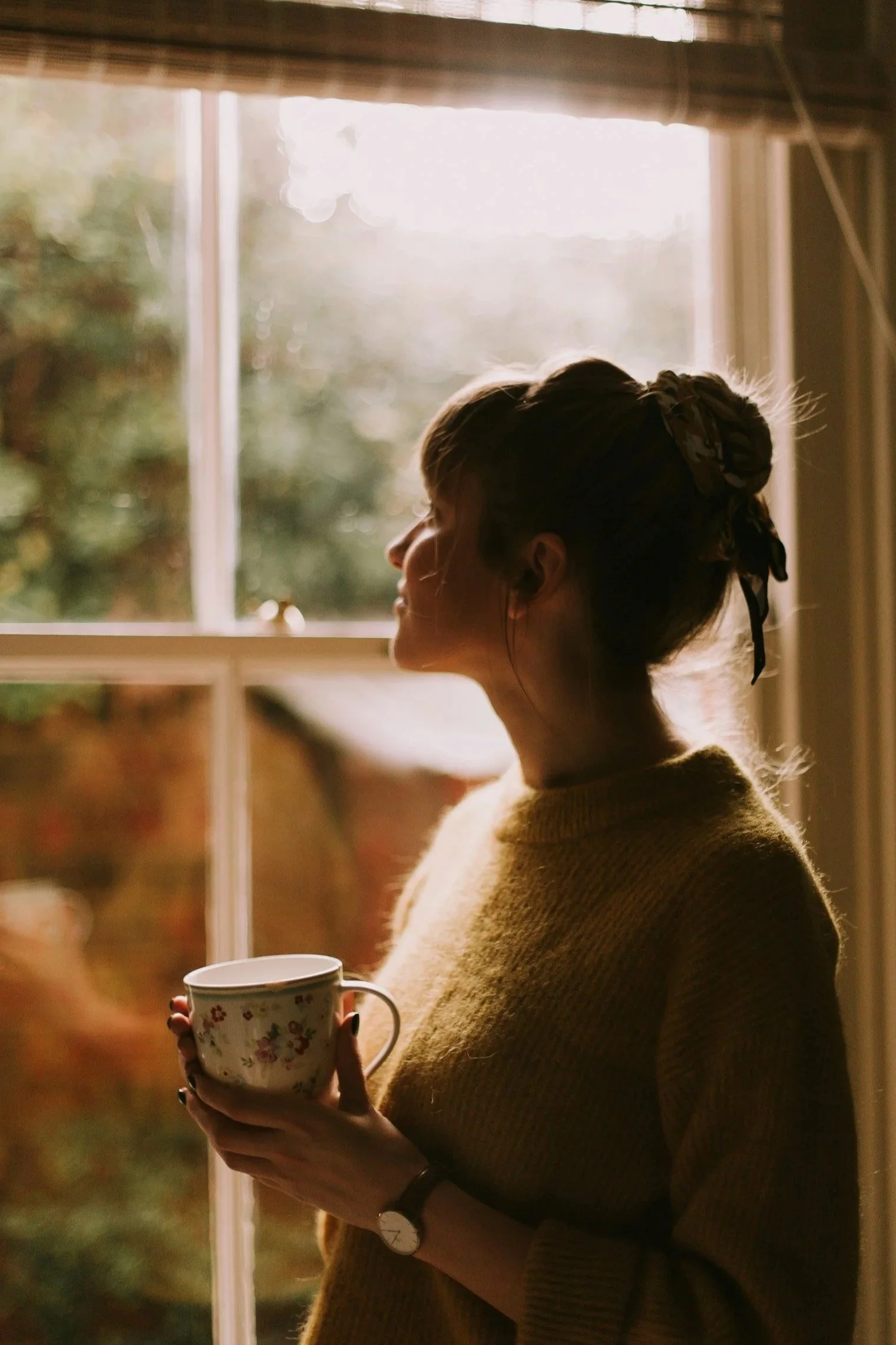 Woman with a warm drink gazing out a window