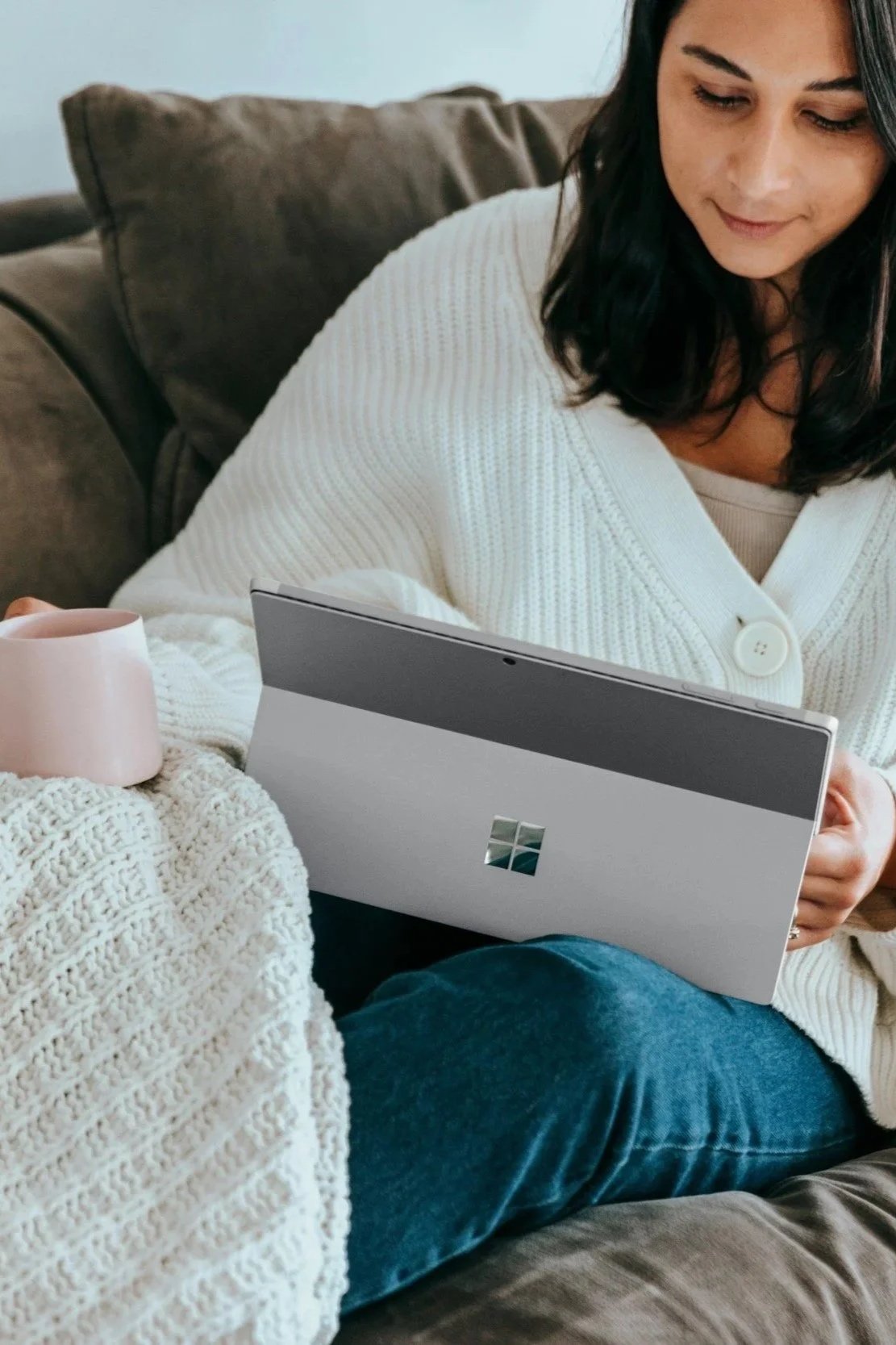 Woman with mug on couch using laptop for online therapy session