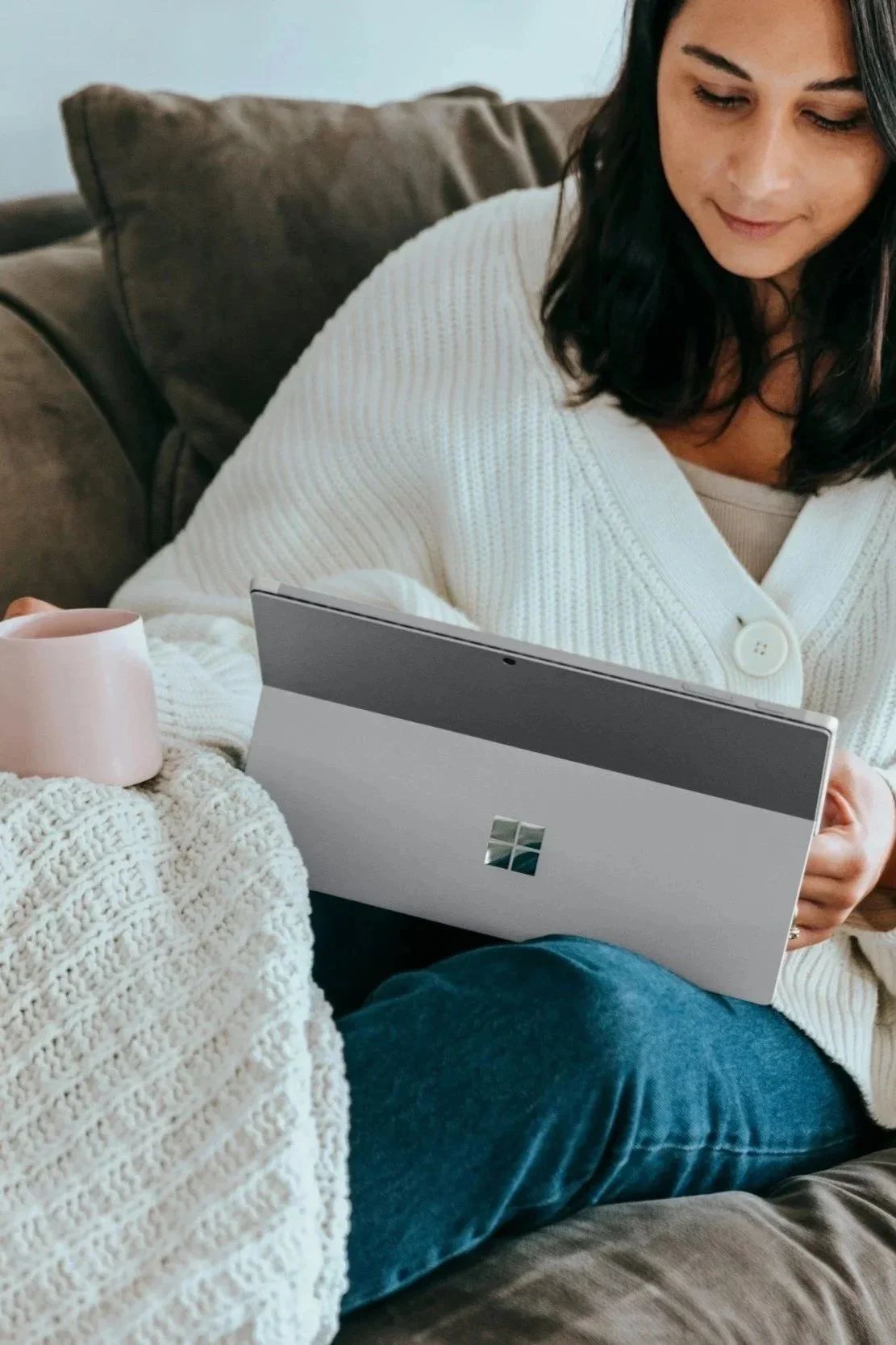 Woman with a mug sitting on a couch using a laptop