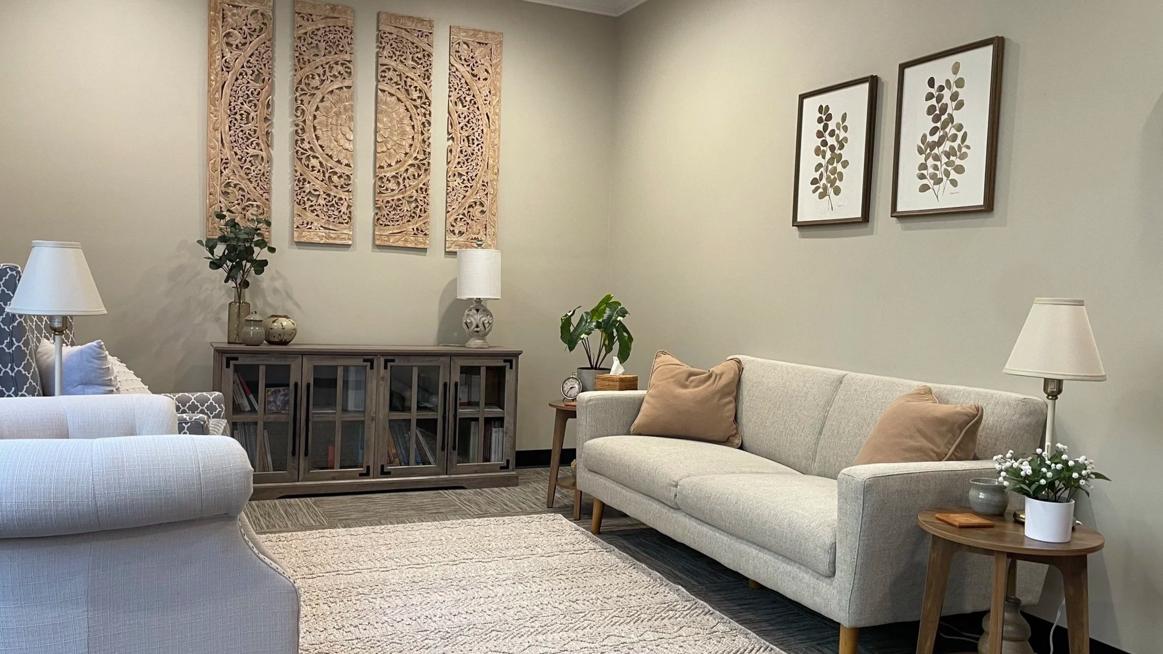 Cozy therapy office with a light gray couch, framed botanical prints, and a plant