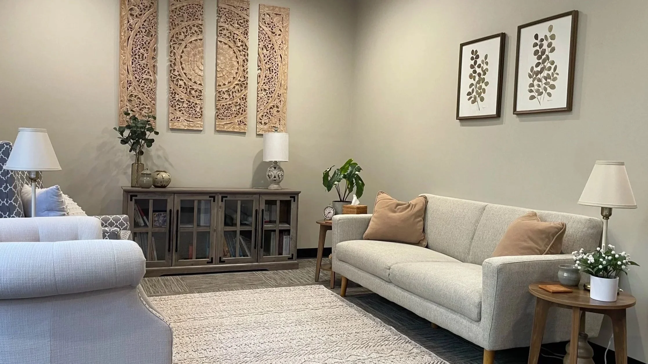 Therapy office with light-toned couches, plants, and framed art