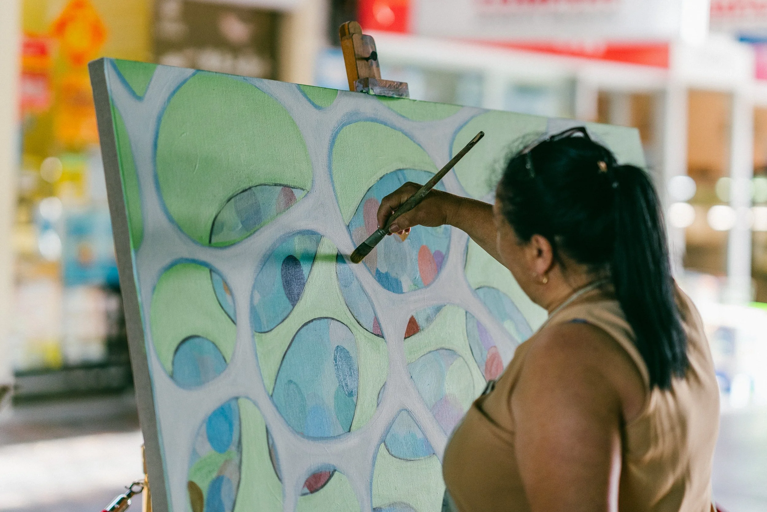 A woman painting on a canvas with colorful, abstract circular designs in an outdoor setting. This painting was part of an intiative by city of Ryde during covid-19 and the Granny Smith festival.