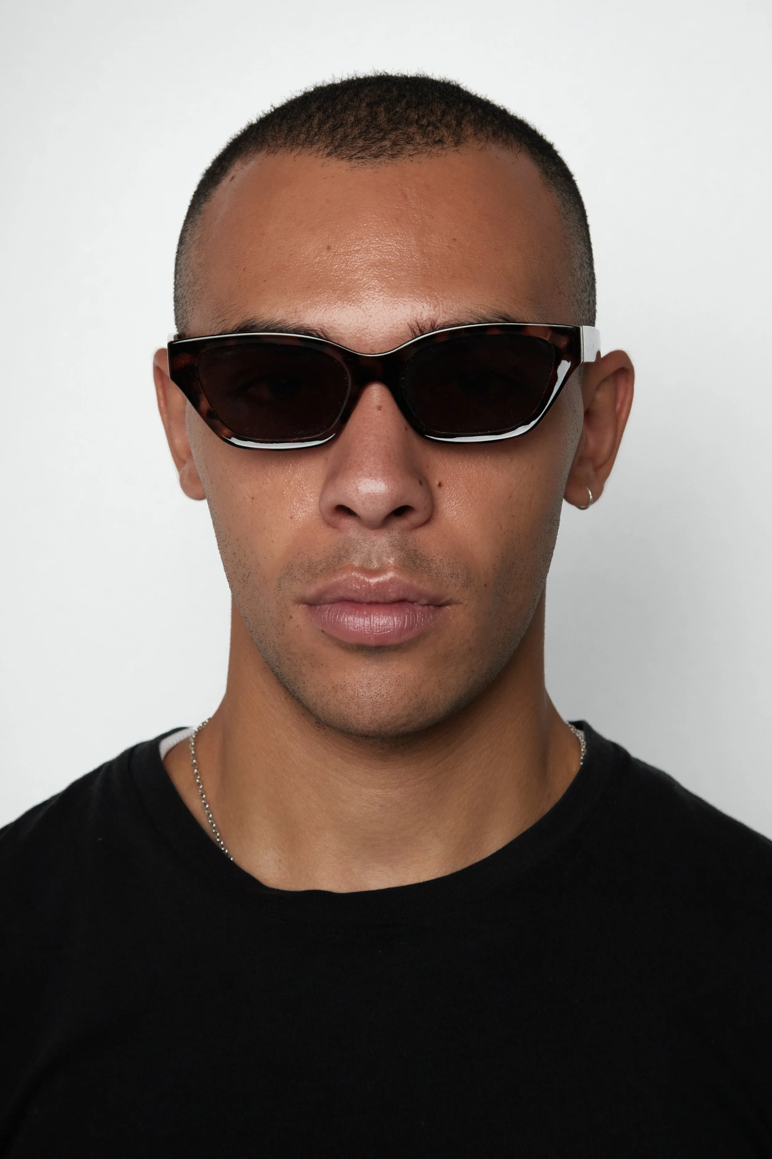 A man in sunglasses and a black shirt stands confidently, exuding a cool and stylish demeanor.