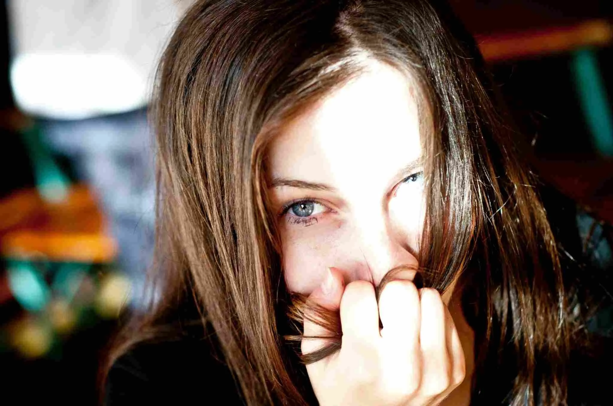 Close-up of a shy woman partly hiding her face behind her hand and hair, gazing intensely at someone with restrained longing
