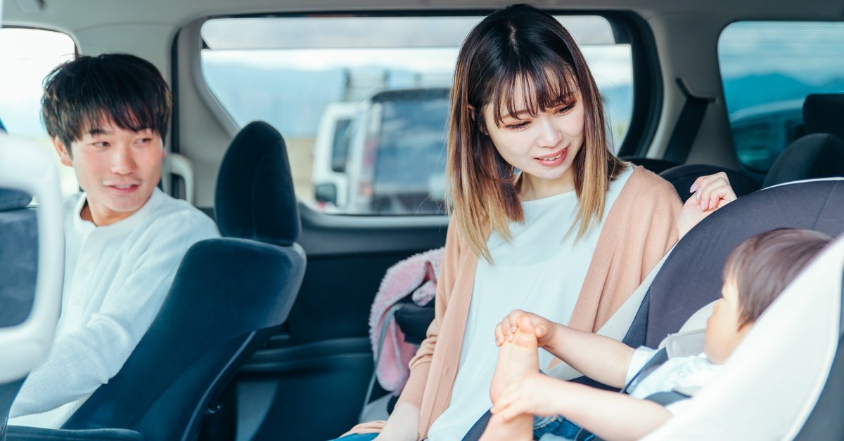 A young father and mother sitting in the back seat of a vehicle with their baby, who’s in a car seat.