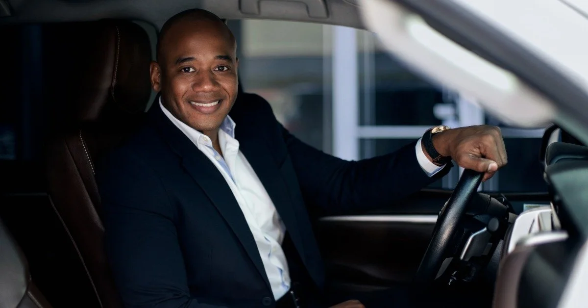 A professional chauffeur in a black suit seated behind the wheel of a vehicle.